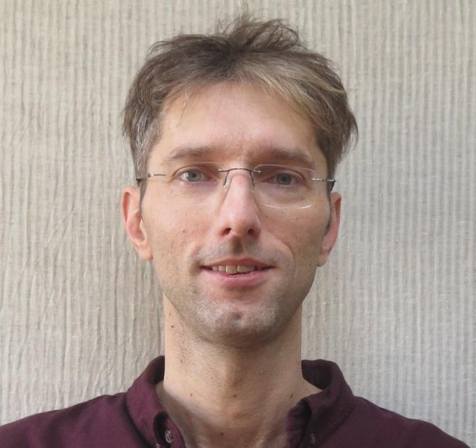 Portrait of Chris Veigl dark and grey hair and wearing glasses and a red shirt.
