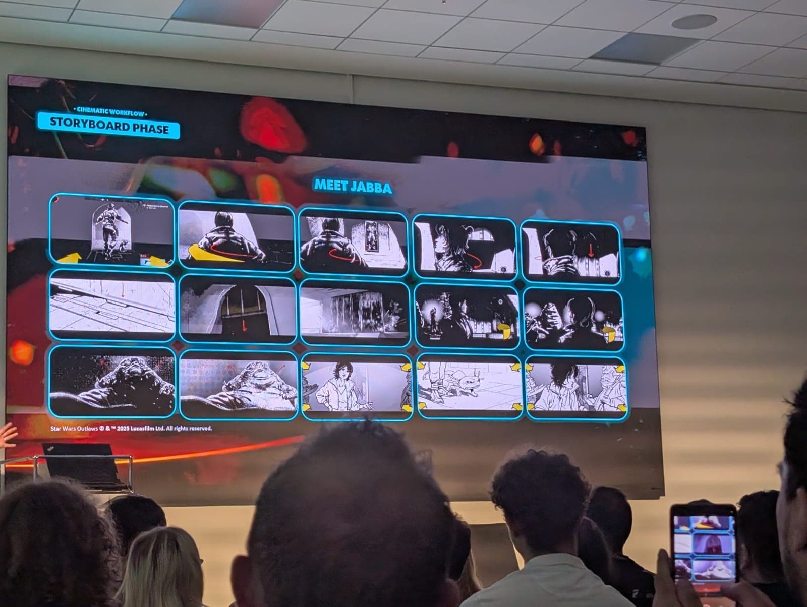 Auf einer Projektionsfläche wird eine Storyboard-Phase mit dem Titel Meet Jabba gezeigt, die 15 schwarz-weiße Storyboard-Tafeln umfasst. Die Zuschauer sitzen mit dem Gesicht zur Leinwand; eine Person macht ein Foto mit ihrem Handy in der unteren rechten Ecke.