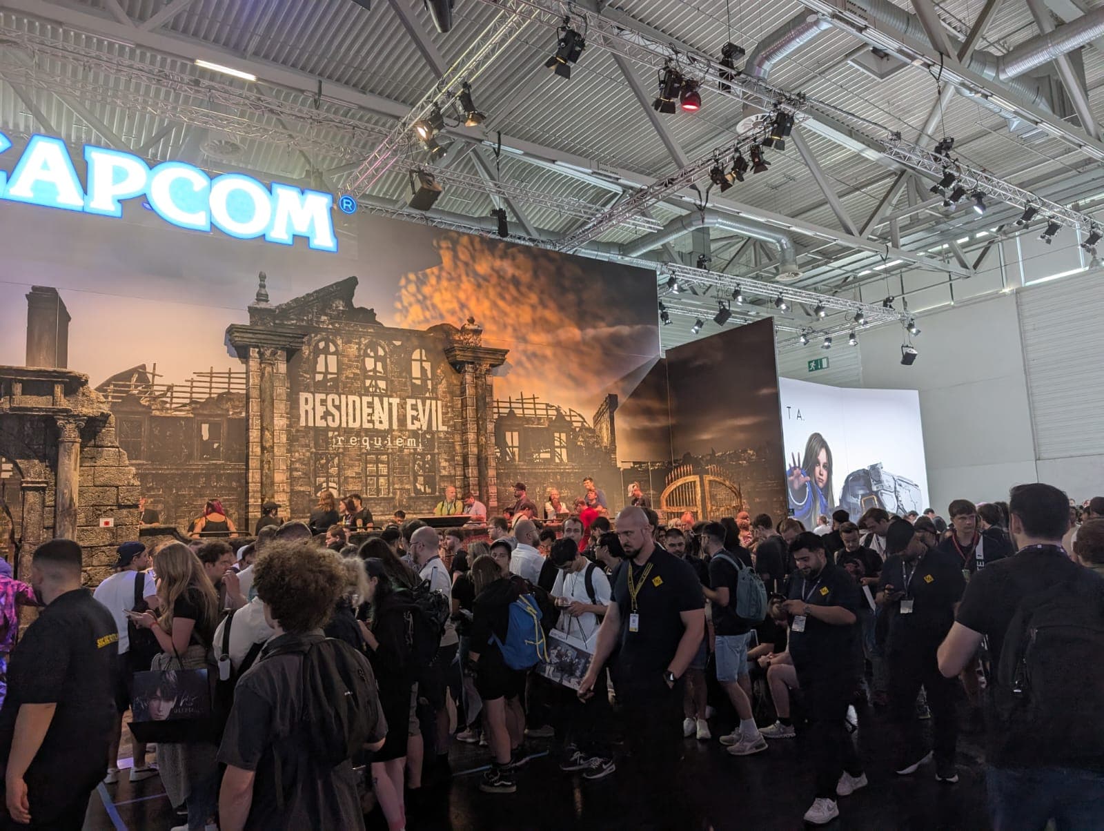 Eine große Menschenmenge versammelt sich am Capcom-Stand während einer Spielemesse, mit einer auffälligen Resident Evil Village-Kulisse und Menschen, die interagieren, Fotos machen und die Veranstaltung erkunden.