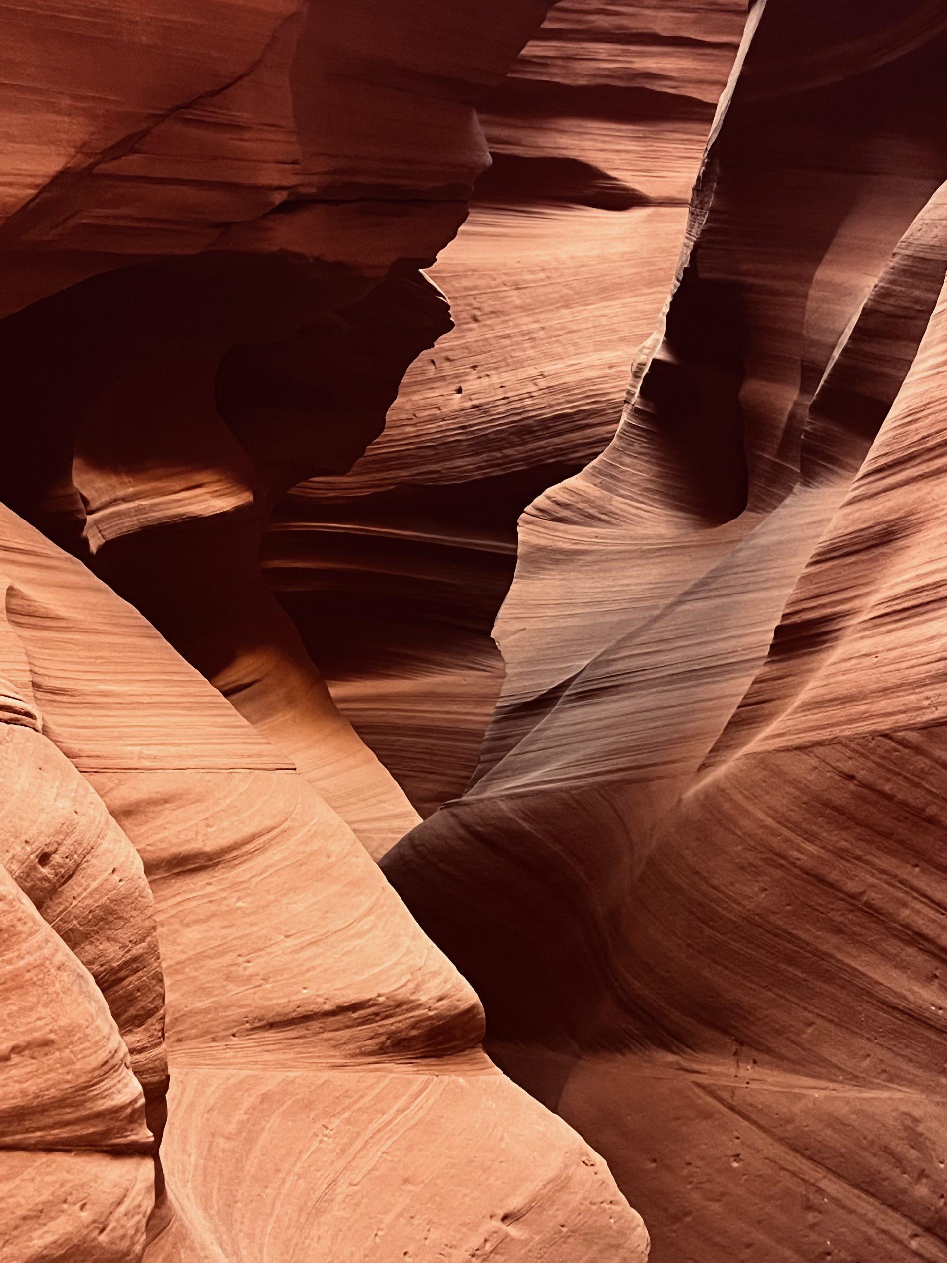 Eine Nahaufnahme von glatten, gewundenen Sandsteinwänden in Orange- und Brauntönen, die enge Durchgänge und geschichtete Strukturen bilden, wahrscheinlich in einem Slot Canyon mit weichem, natürlichem Licht.