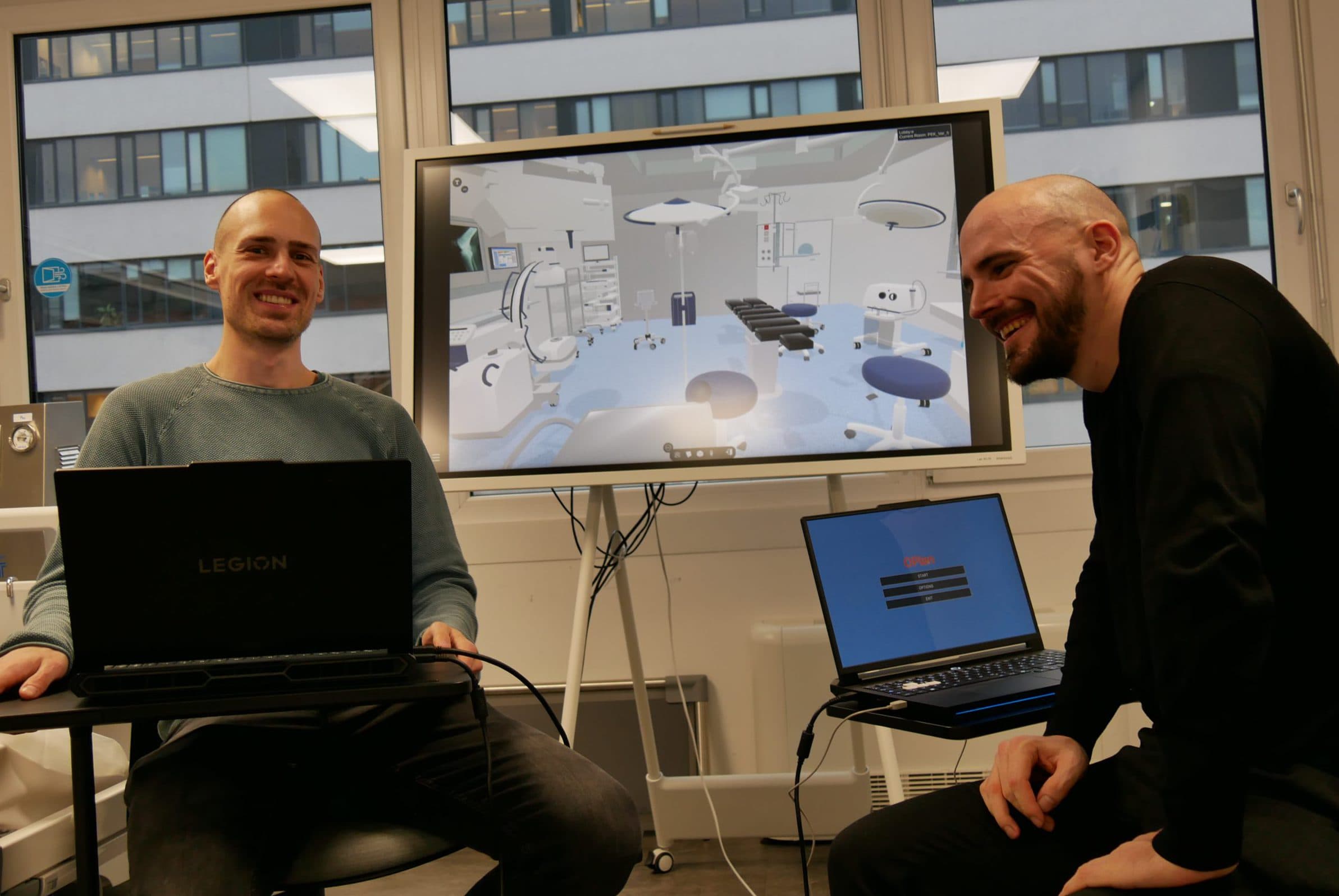Zwei lächelnde Männer sitzen mit Laptops vor einem großen Bildschirm, auf dem ein 3D-Modell eines Krankenhauszimmers oder eines medizinischen Labors zu sehen ist. Große Fenster hinter ihnen zeigen ein Bürogebäude. Die Atmosphäre wirkt kooperativ und freundlich.
