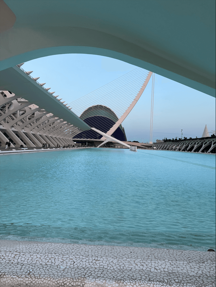 Ein Blick auf einen modernen architektonischen Komplex mit weißen geometrischen Strukturen, einem großen Pool mit türkisfarbenem Wasser und dem LHemisfèric-Gebäude im Hintergrund in der Stadt der Künste und Wissenschaften in Valencia, Spanien.