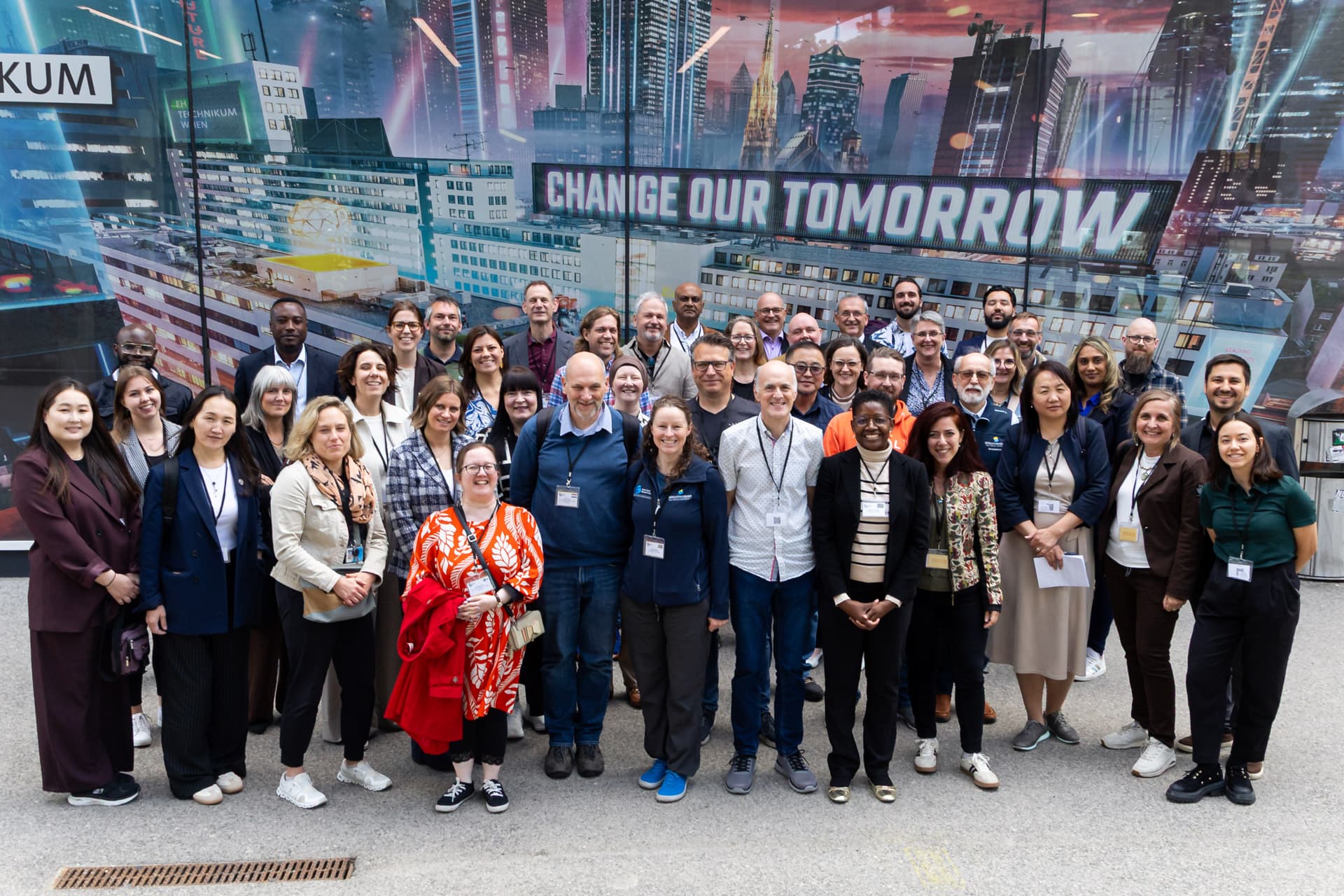 Eine große Gruppe von Menschen steht zusammen und lächelt für ein Foto vor einer futuristischen Wandmalerei mit der Aufschrift CHANGE OUR TOMORROW im Hintergrund.