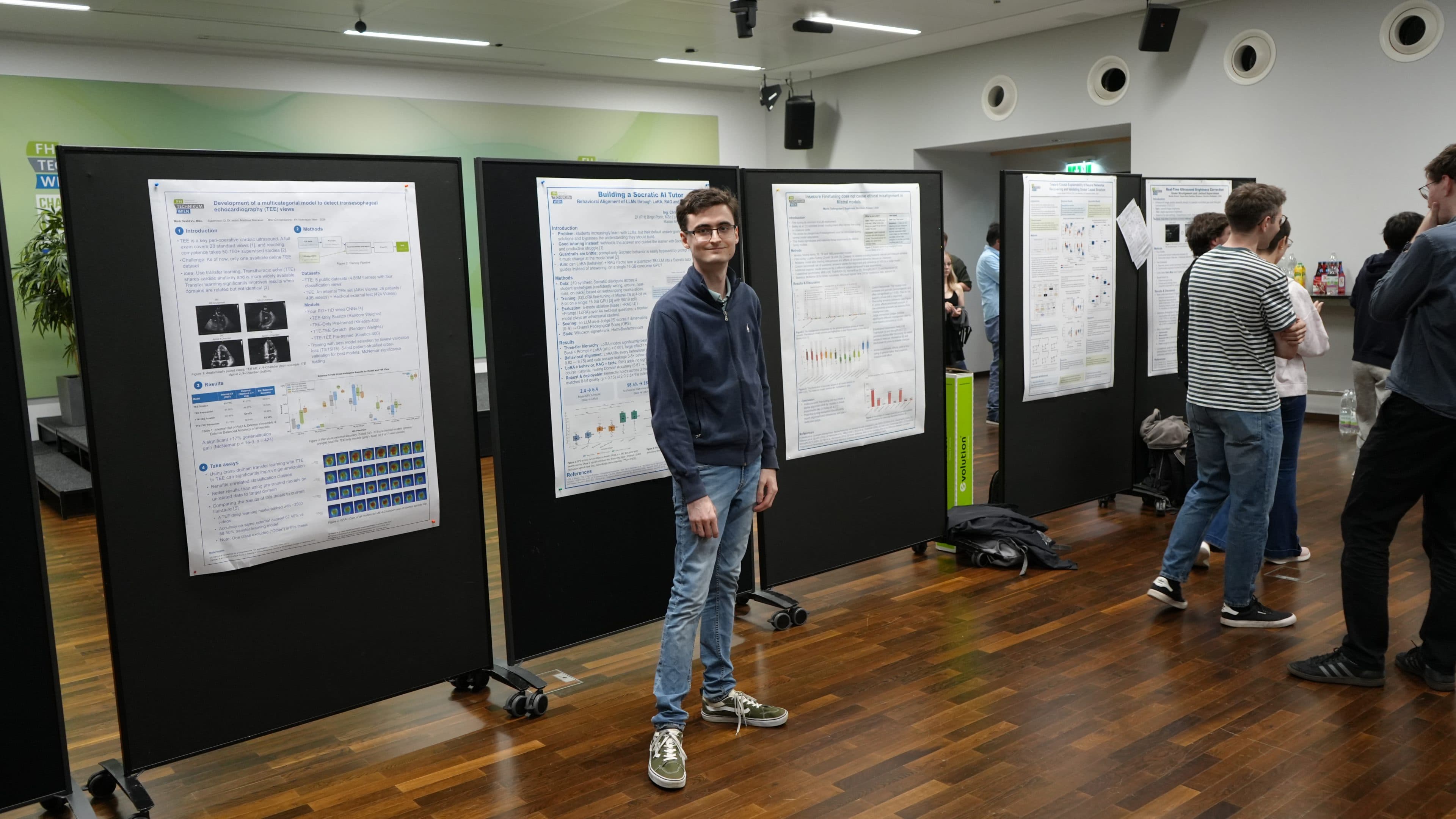 Auf einer Wissenschaftskonferenz steht eine Person vor Forschungsplakaten, die an schwarzen Tafeln angebracht sind. Im Hintergrund betrachten andere Teilnehmer die Plakate und unterhalten sich. Der Boden ist aus Holz, und die Szene scheint in einem Innenraum zu spielen.