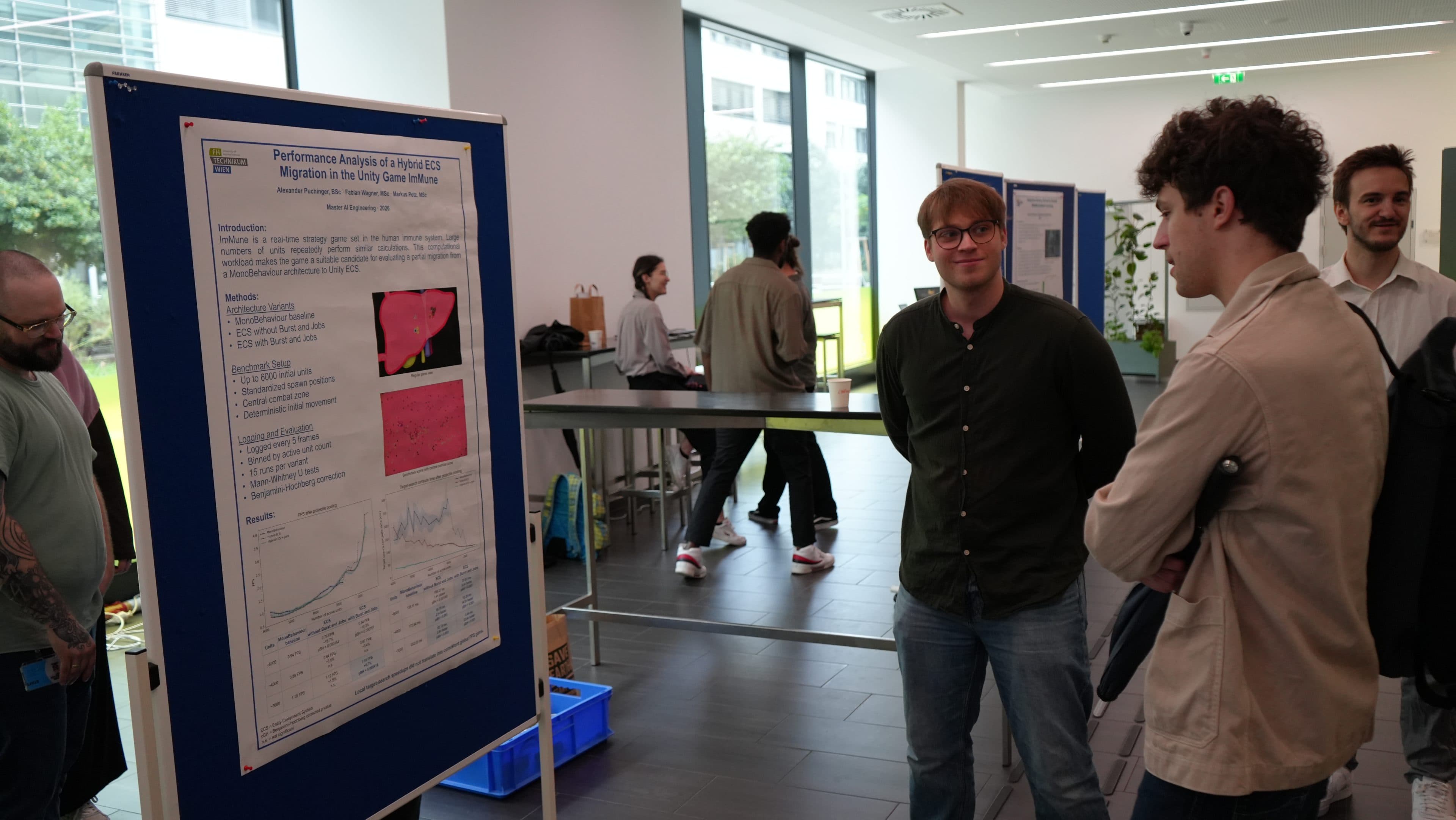 Bei einer Veranstaltung in einem Saal stehen zwei Personen vor einem wissenschaftlichen Poster und diskutieren dessen Inhalt. Im Hintergrund sind weitere Personen zu sehen, von denen einige sich unterhalten und andere umhergehen. Die Atmosphäre wirkt ungezwungen und akademisch.