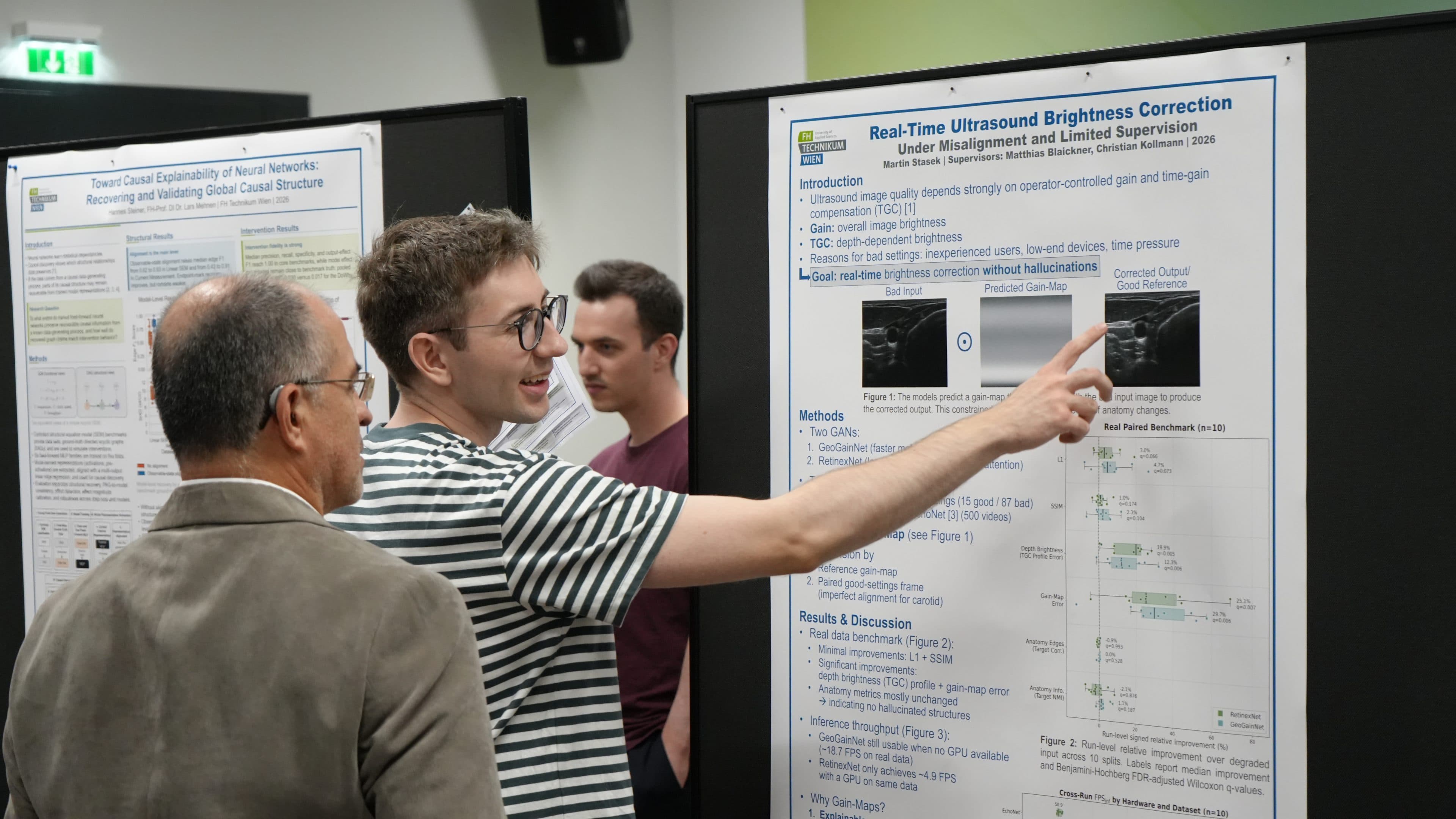 Ein junger Mann erklärt einem älteren Mann auf einer Konferenz begeistert ein wissenschaftliches Poster und zeigt dabei auf einen bestimmten Abschnitt. Ein weiterer Teilnehmer steht in der Nähe und betrachtet ebenfalls die ausgestellten Poster.