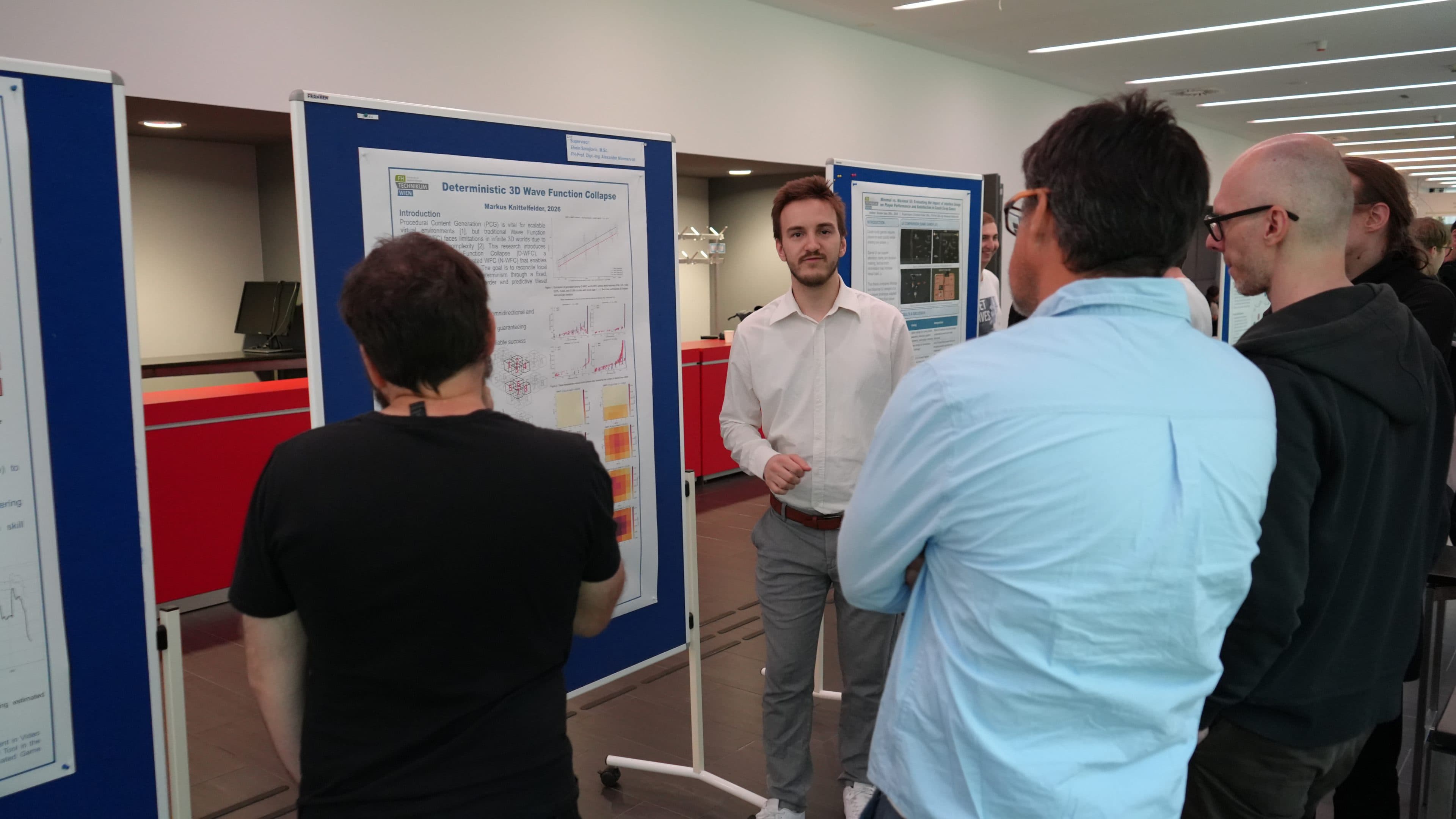 Ein Mann in einem weißen Hemd präsentiert vier Personen, die sich um ihn versammelt haben, ein wissenschaftliches Poster in einem modernen, hell erleuchteten Raum, im Hintergrund sind blaue Ausstellungstafeln und rote Wände zu sehen.