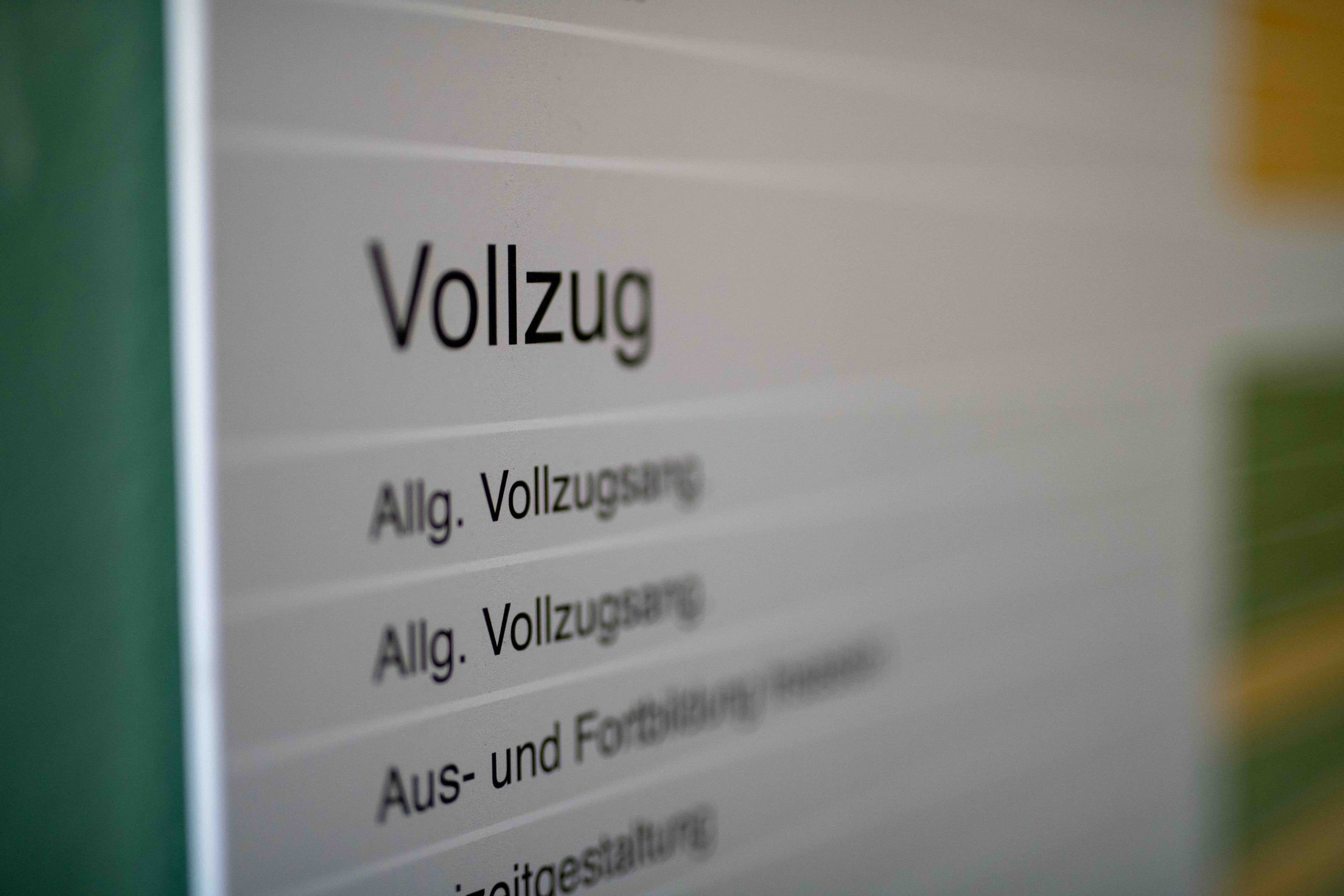 Nahaufnahme eines Schildes auf Deutsch, auf dem oben das Wort „Vollzug“ steht, gefolgt von einer Liste von Kategorien, darunter „Allg. Vollzugsang“ und „Aus- und Fortbildung“. Der Text erscheint leicht unscharf.