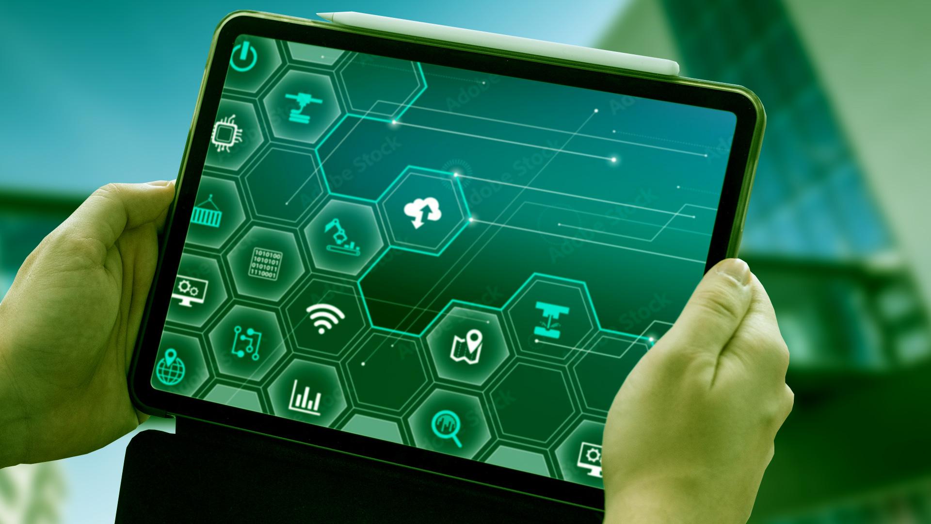 Eine Person hält ein Tablet mit grünen, sechseckigen Symbolen aus den Bereichen Technologie, Cloud Computing und Konnektivität in der Hand, mit einem unscharfen modernen Gebäude im Hintergrund.