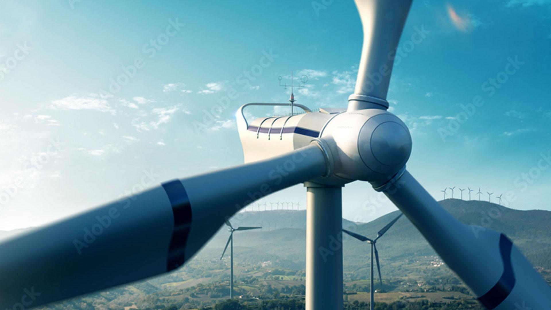 Nahaufnahme einer Windturbine vor einem klaren blauen Himmel, mit einigen weiteren Windturbinen und grünen Hügeln im Hintergrund.