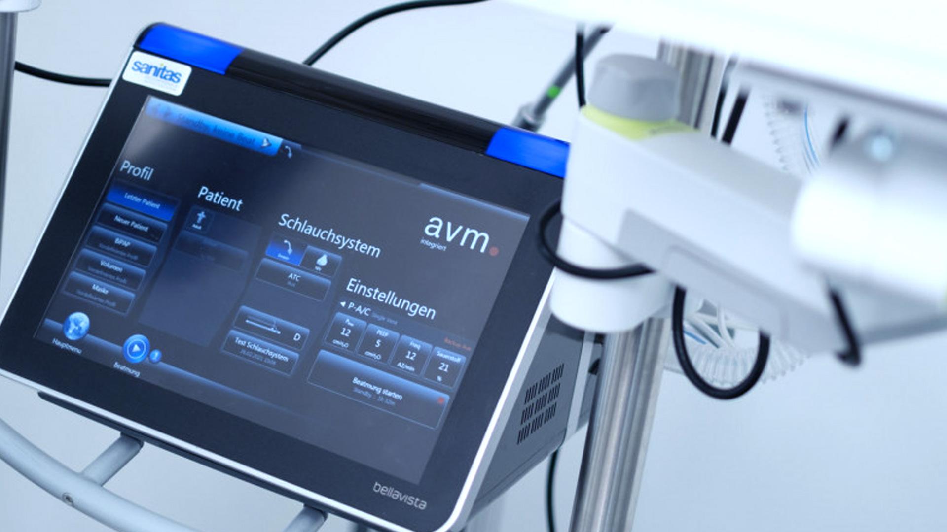 Nahaufnahme eines Touchscreens für ein medizinisches Gerät, auf dem Einstellungen und Patienteninformationen angezeigt werden und um den herum verschiedene Bedienelemente und Kabel zu sehen sind. Die Benutzeroberfläche ist in deutscher Sprache und zeigt Optionen zur Einstellung des Systems an.