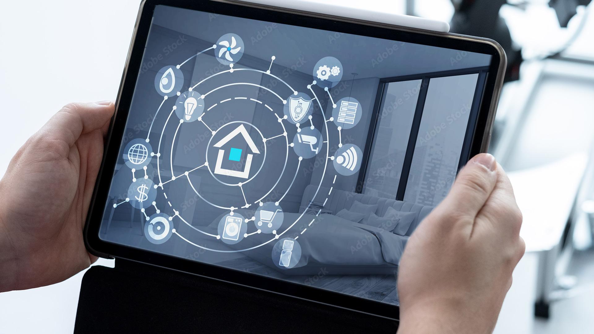 Eine Person hält ein Tablet in der Hand, auf dem eine Smart-Home-Benutzeroberfläche mit Symbolen für vernetzte Geräte wie Beleuchtung, Thermostat, Sicherheitssysteme und Haushaltsgeräte vor dem Hintergrund eines modernen Schlafzimmers angezeigt wird.