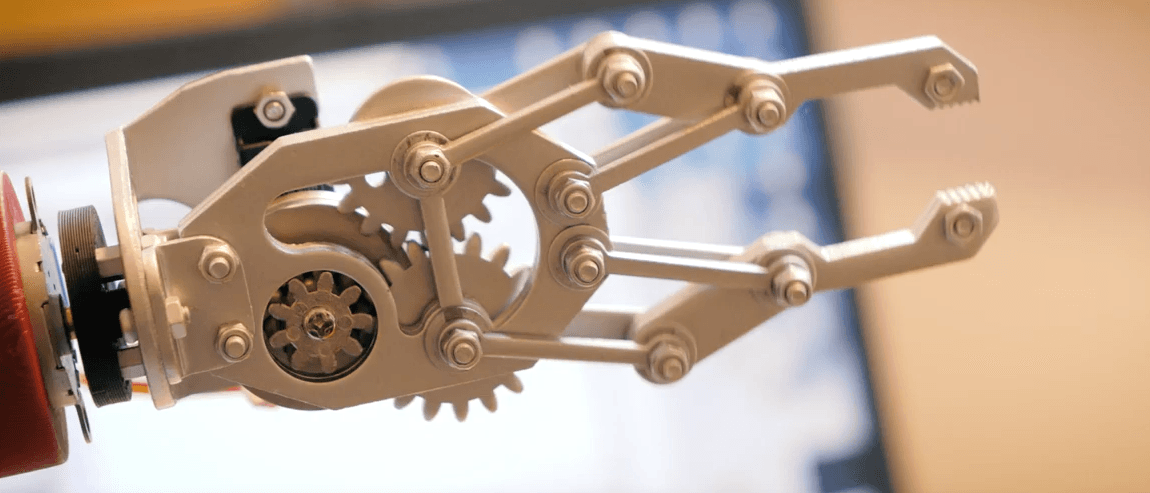 Nahaufnahme einer mechanischen Roboterhand aus Metall, mit Zahnrädern und Gelenken, mit unscharfem Hintergrund.