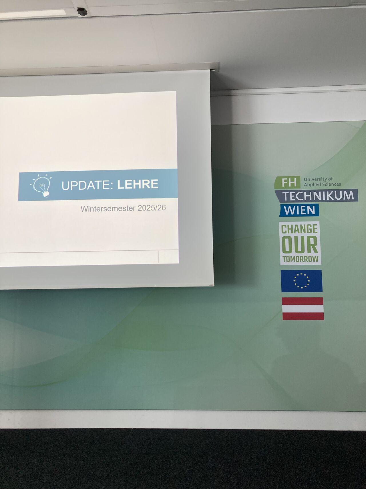Auf einer Präsentationsfolie steht UPDATE: LEHRE Wintersemester 2025/26. An der Wand daneben hängen Logos der FH Technikum Wien, Change Our Tomorrow und die österreichische Flagge.
