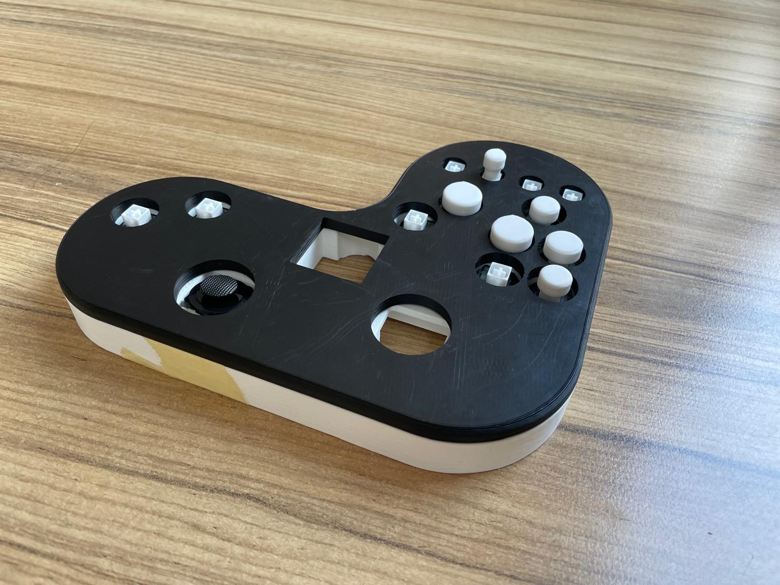 Ein kundenspezifischer, teilweise zusammengebauter Game-Controller mit schwarzer Oberseite und weißen Tasten, der auf einer Holzoberfläche ruht. Der Controller hat ein ungewöhnliches Layout mit einer großen Aussparung und freiliegenden Komponenten.