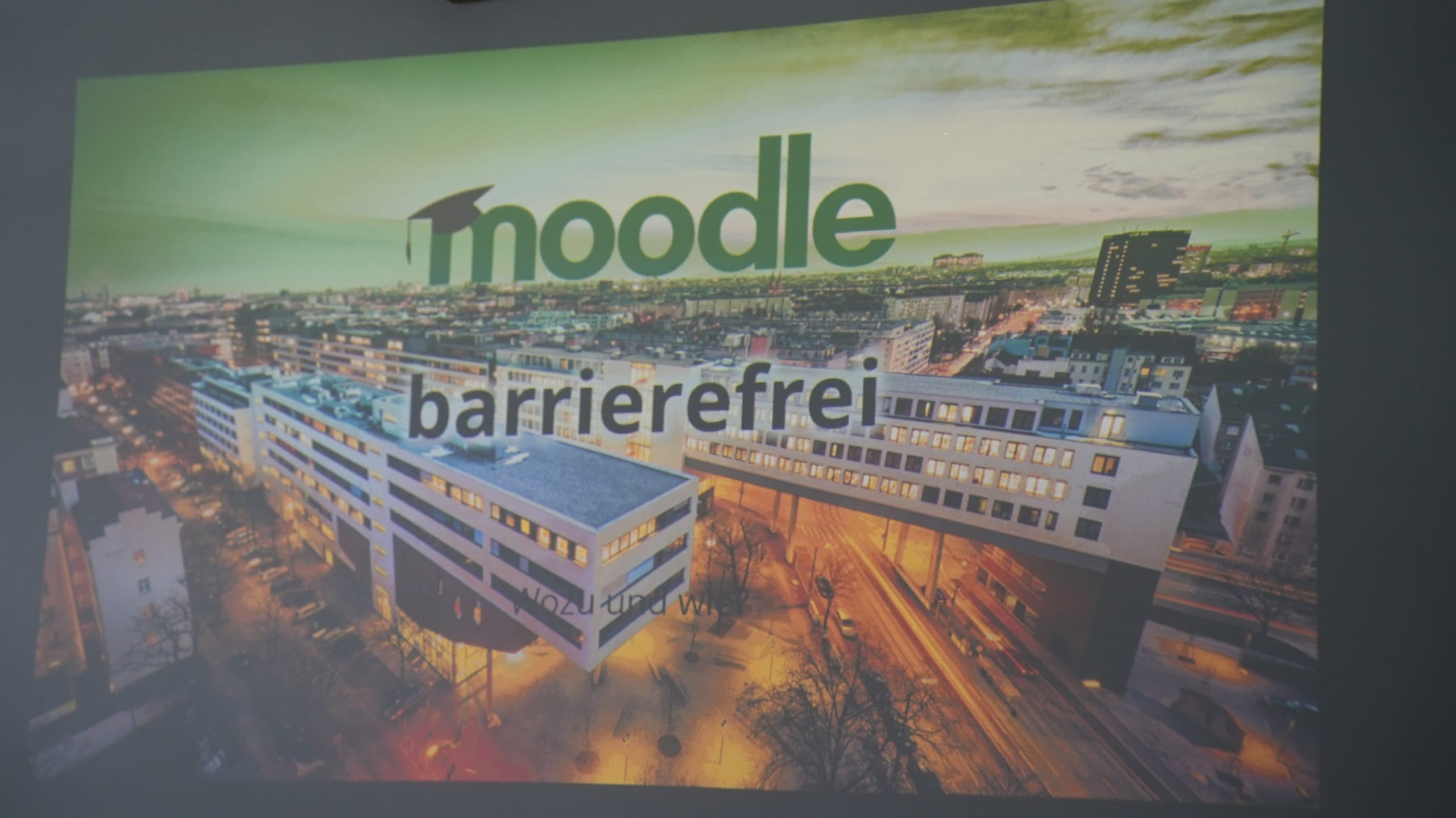 Eine Stadtlandschaft bei Sonnenuntergang mit großen weißen Gebäuden im Vordergrund. Der Schriftzug Moodle barrierefrei ist eingeblendet und weist auf eine barrierefreie Version der Moodle-Plattform hin.