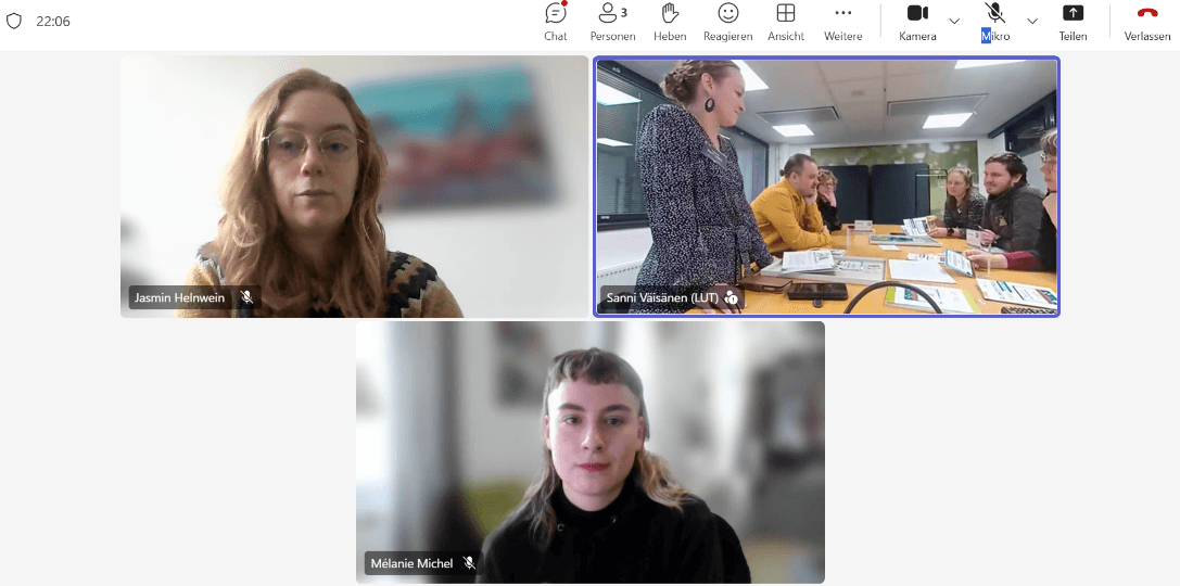 Eine Videokonferenz zeigt drei Panels: eines mit einer Frau mit Brille, die spricht, eines mit einer Gruppe von Personen in einem Besprechungsraum und eines mit einer Frau in einem dunklen Pullover. Unter jedem Teilnehmer werden die Namen angezeigt.