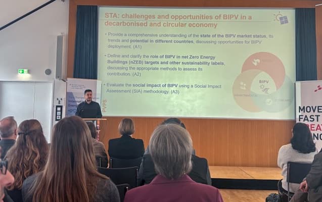 Ein Redner hält einen Vortrag vor einem Publikum in einem Konferenzraum. Hinter ihm erörtert eine Folie die Herausforderungen und Chancen von BIPV in einer dekarbonisierten Wirtschaft und listet Punkte zum Marktstatus, zur Politik und zur Bewertung der sozialen Auswirkungen auf.