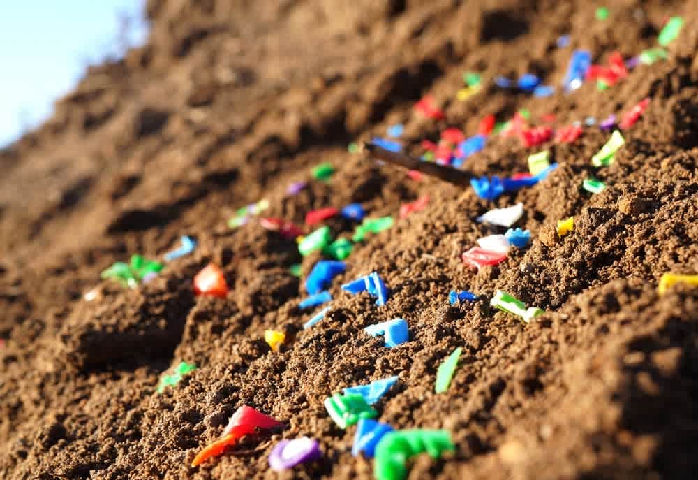 Auf dem braunen Boden verstreut liegen bunte Plastikabfälle, die auf Umweltverschmutzung und Umweltprobleme hinweisen.