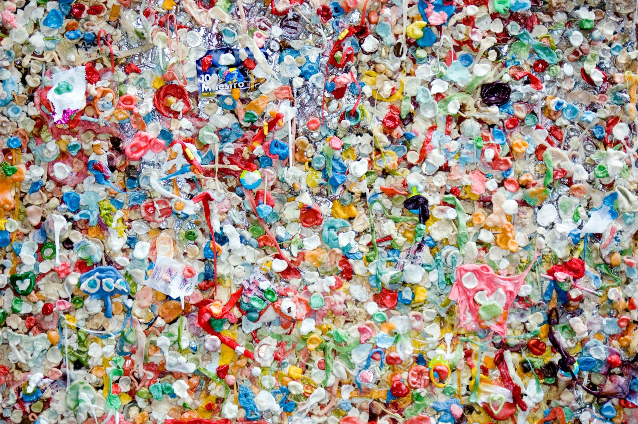 Eine dichte Wand, bedeckt mit gekauten, bunten Kaugummistücken in verschiedenen Formen und Größen, die ein lebendiges und chaotisches Mosaikmuster bilden.