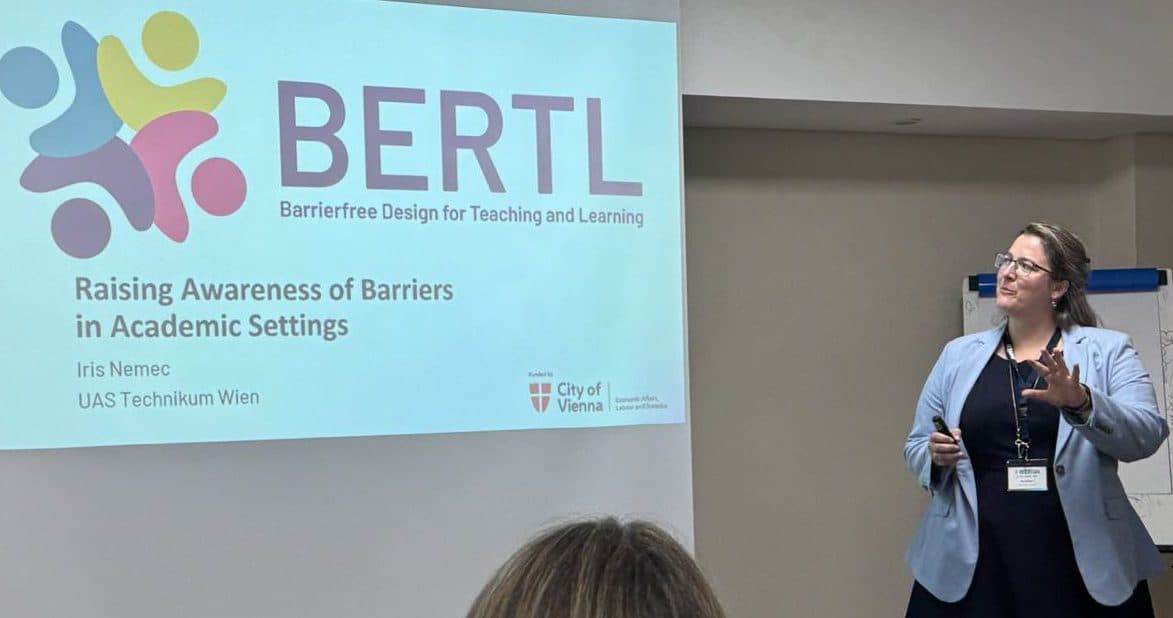 Eine Frau in einem blauen Blazer steht vor einer Leinwand, auf der eine Präsentation mit dem Titel „BERTL: Barrierefreies Design für Lehre und Lernen“ zu sehen ist, die sich mit Barrieren im akademischen Umfeld befasst, und hält eine Rede.