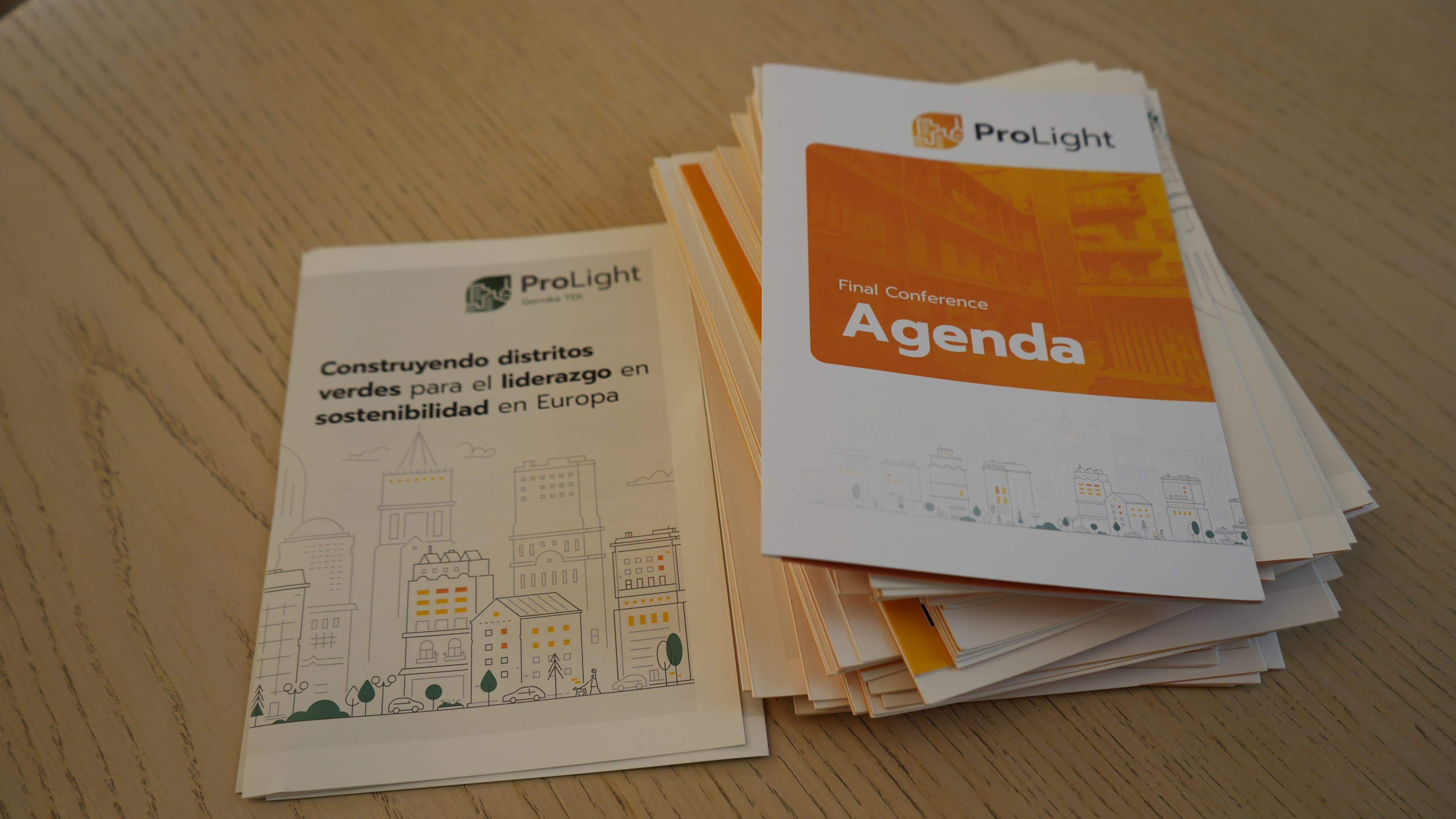 Auf einem Holztisch liegen zwei Broschüren: eine auf Spanisch über den Bau umweltfreundlicher Stadtviertel im Sinne der Nachhaltigkeit in Europa und eine weitere mit dem Programm der ProLight-Abschlusskonferenz, darunter sind weitere Broschüren gestapelt.