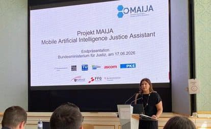 Eine Frau steht am Rednerpult und hält einen Vortrag über das Projekt „Mobile Artificial Intelligence Justice Assistant“. Hinter ihr sind auf einer großen Leinwand der Projekttitel und die Logos zu sehen, während das Publikum aufmerksam zuhört.