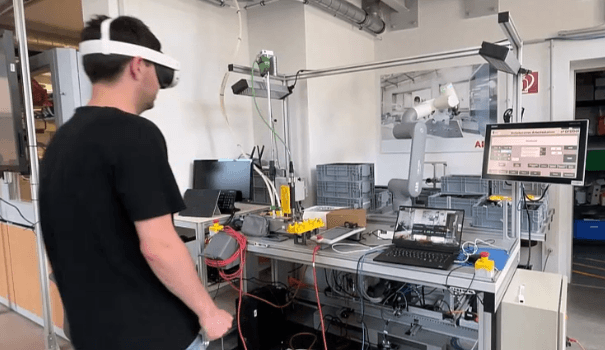 Eine Person, die ein VR-Headset trägt, steht vor einem Arbeitsplatz mit Kabeln, Computern und Monitoren in einer modernen industriellen Laborumgebung.