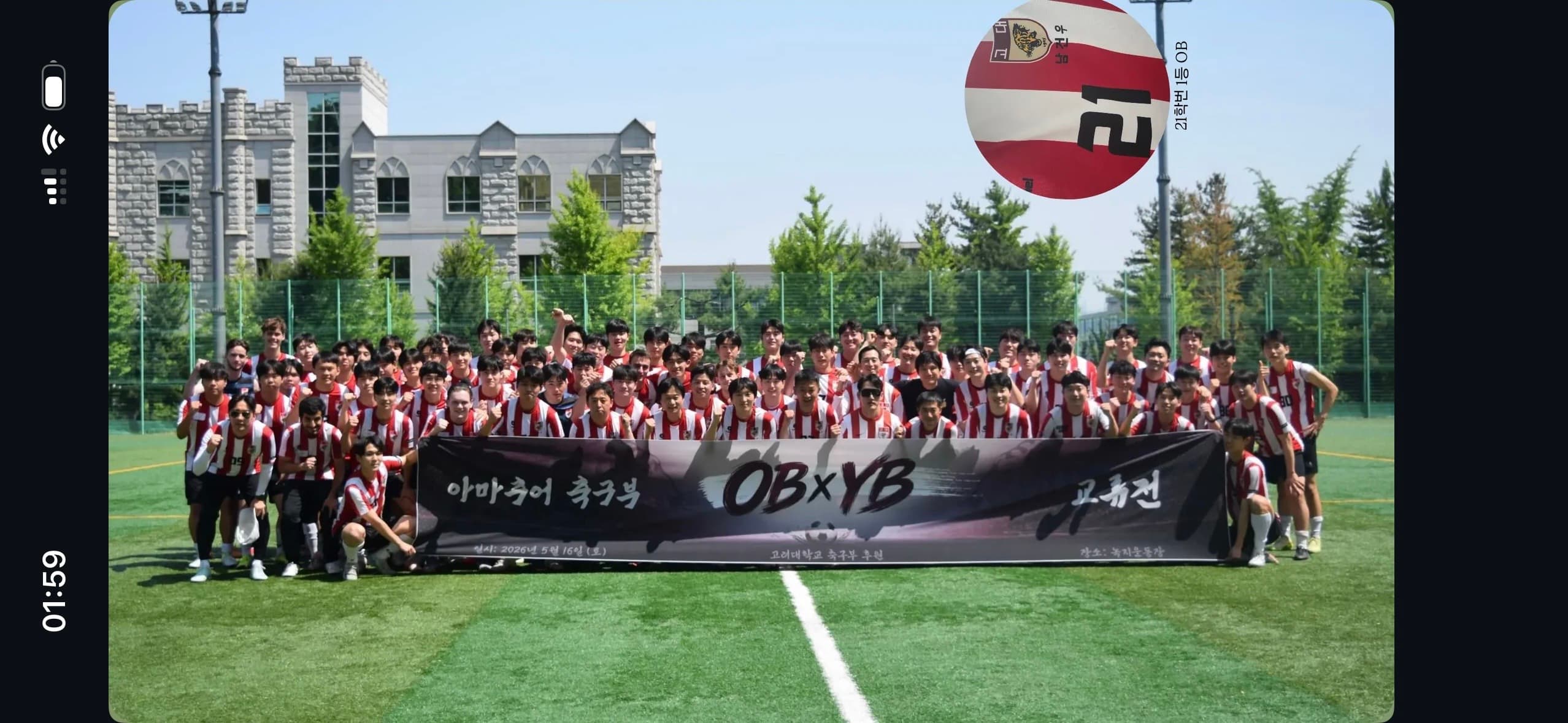 Eine große Gruppe von Menschen in einheitlichen Fußballtrikots posiert auf einem Spielfeld und hält ein schwarzes Transparent mit einer Aufschrift hoch. Über ihnen schwebt ein großer Fußball. Im Hintergrund sind Bäume und ein Steingebäude zu sehen.