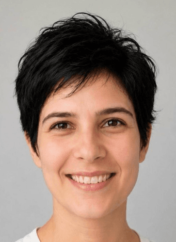 Eine Person mit kurzen, dunklen Haaren und heller Haut lächelt vor einem schlichten hellgrauen Hintergrund in die Kamera.