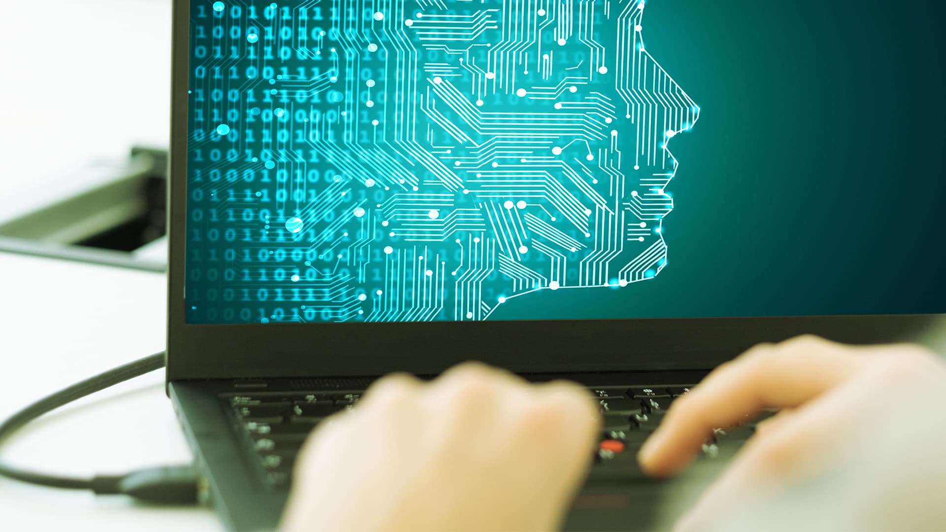 Eine Person tippt auf einem Laptop, auf dessen Bildschirm ein digitales menschliches Gesicht aus Schaltkreisen zu sehen ist, das für künstliche Intelligenz oder Technologie steht.