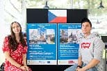 Zwei junge Erwachsene sitzen vor Plakaten mit Texten und Bildern zum Thema Auslandsstudium; über den Plakaten ist eine tschechische Flagge zu sehen.