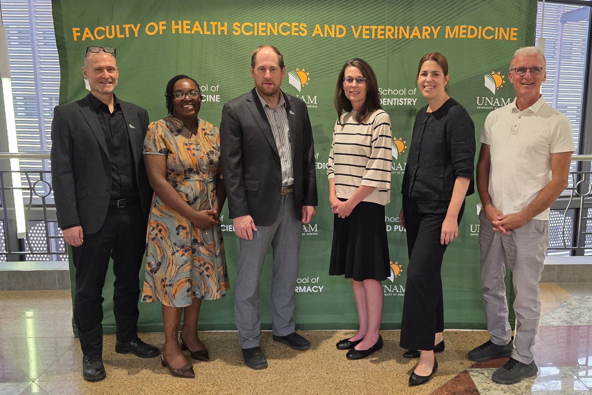 Sechs Personen stehen vor einem grünen Banner der Fakultät für Gesundheitswissenschaften und Veterinärmedizin der UNAM. Sie tragen Business- oder Smart-Casual-Kleidung und lächeln in die Kamera.