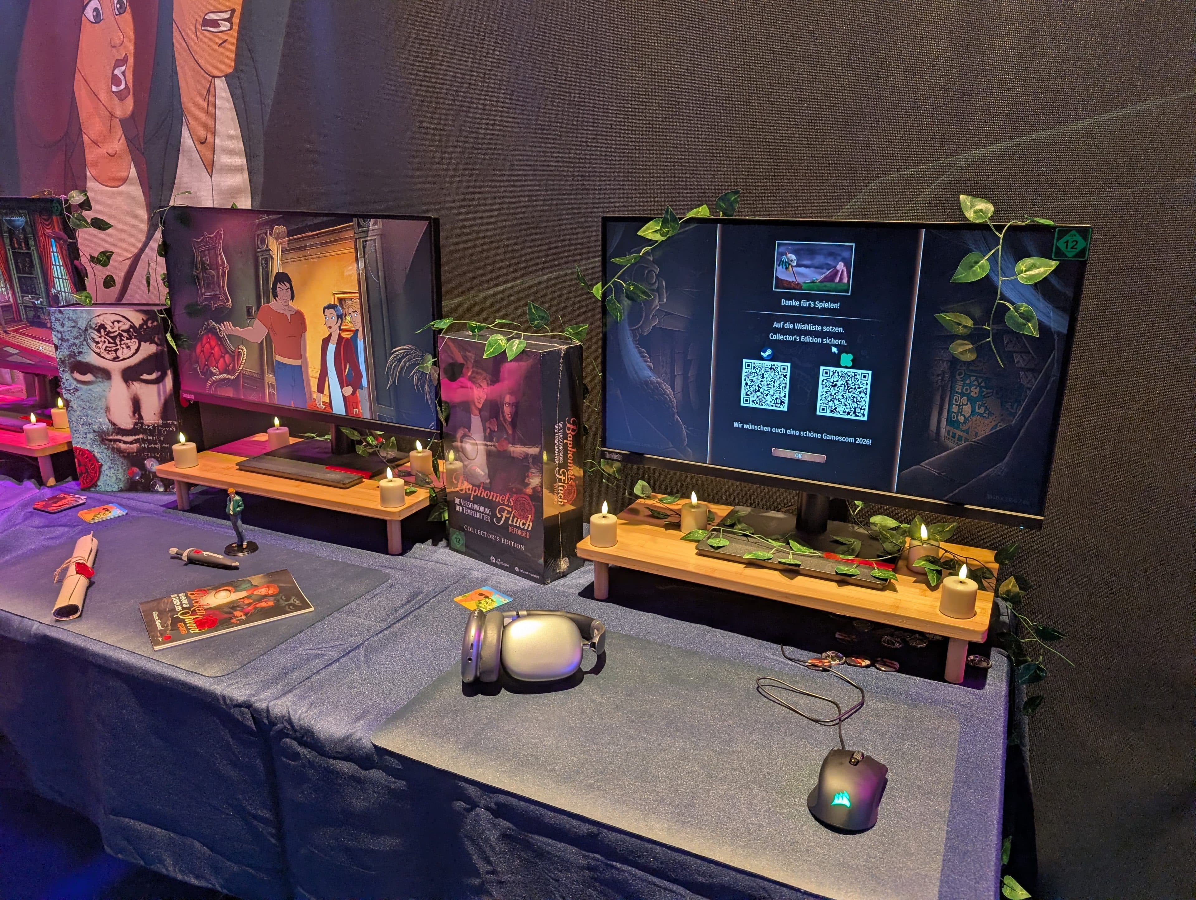 Zwei Computerarbeitsplätze mit Monitoren auf Holzständern, geschmückt mit künstlichen grünen Ranken, VR-Headset, Maus und Spielutensilien auf einer blauen Tischdecke unter warmer Beleuchtung.