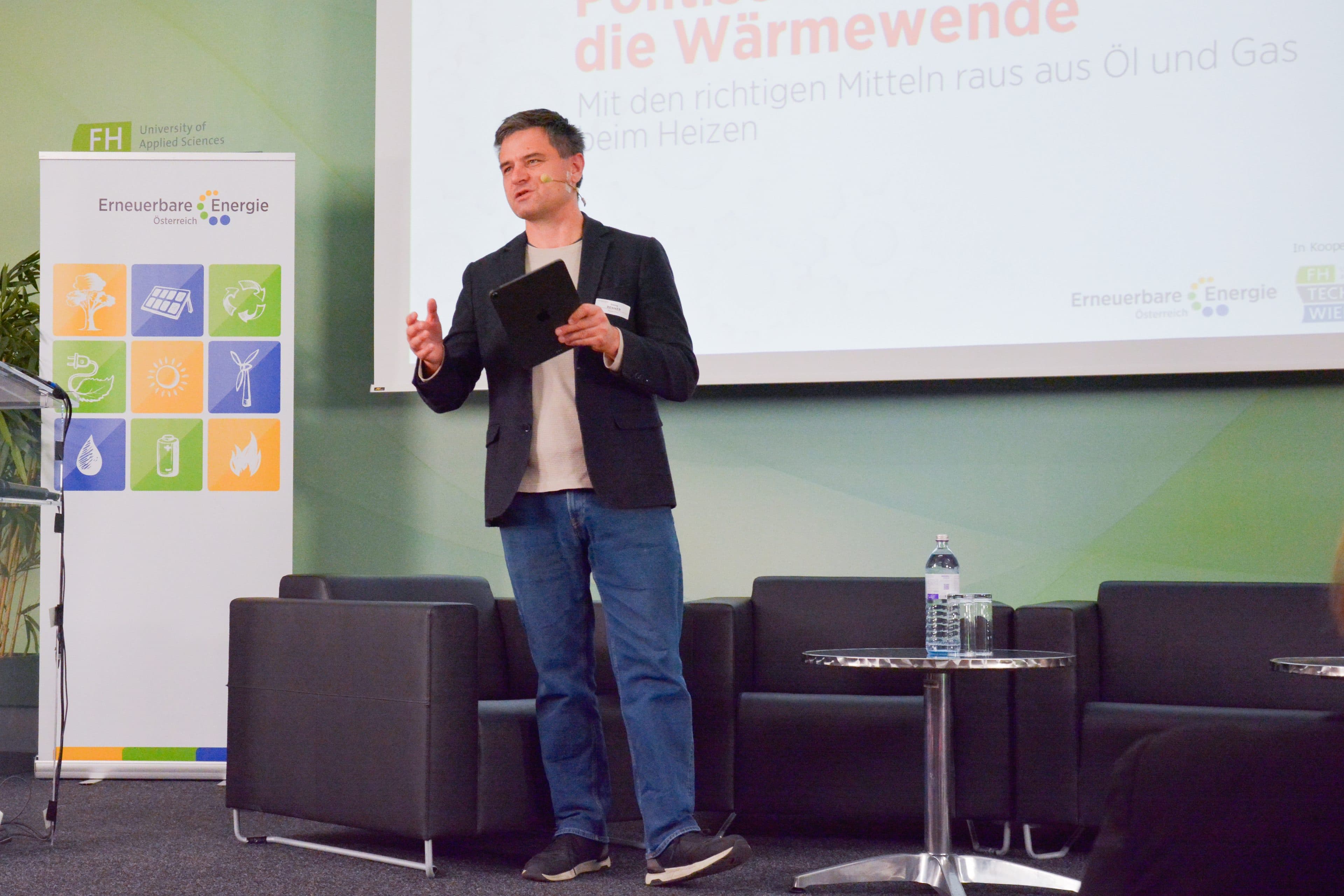 Ein Mann in Blazer und Jeans steht mit einem Tablet in der Hand auf der Bühne und hält vor einer Präsentation über die Energiewende und erneuerbare Energien eine Rede.