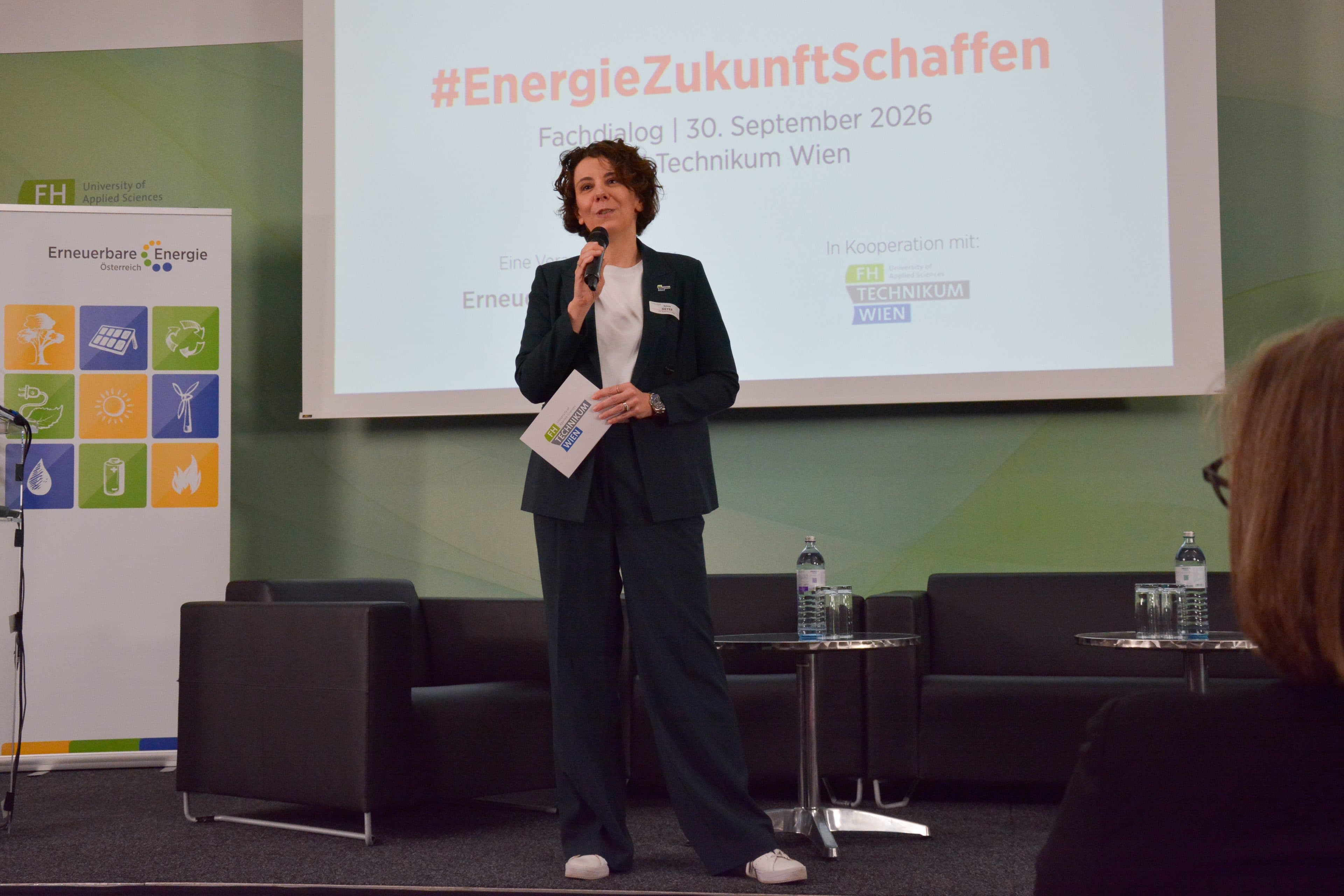 Eine Frau, die auf der Bühne vor einer Präsentationsleinwand mit der Aufschrift #EnergieZukunftSchaffen in ein Mikrofon spricht.
