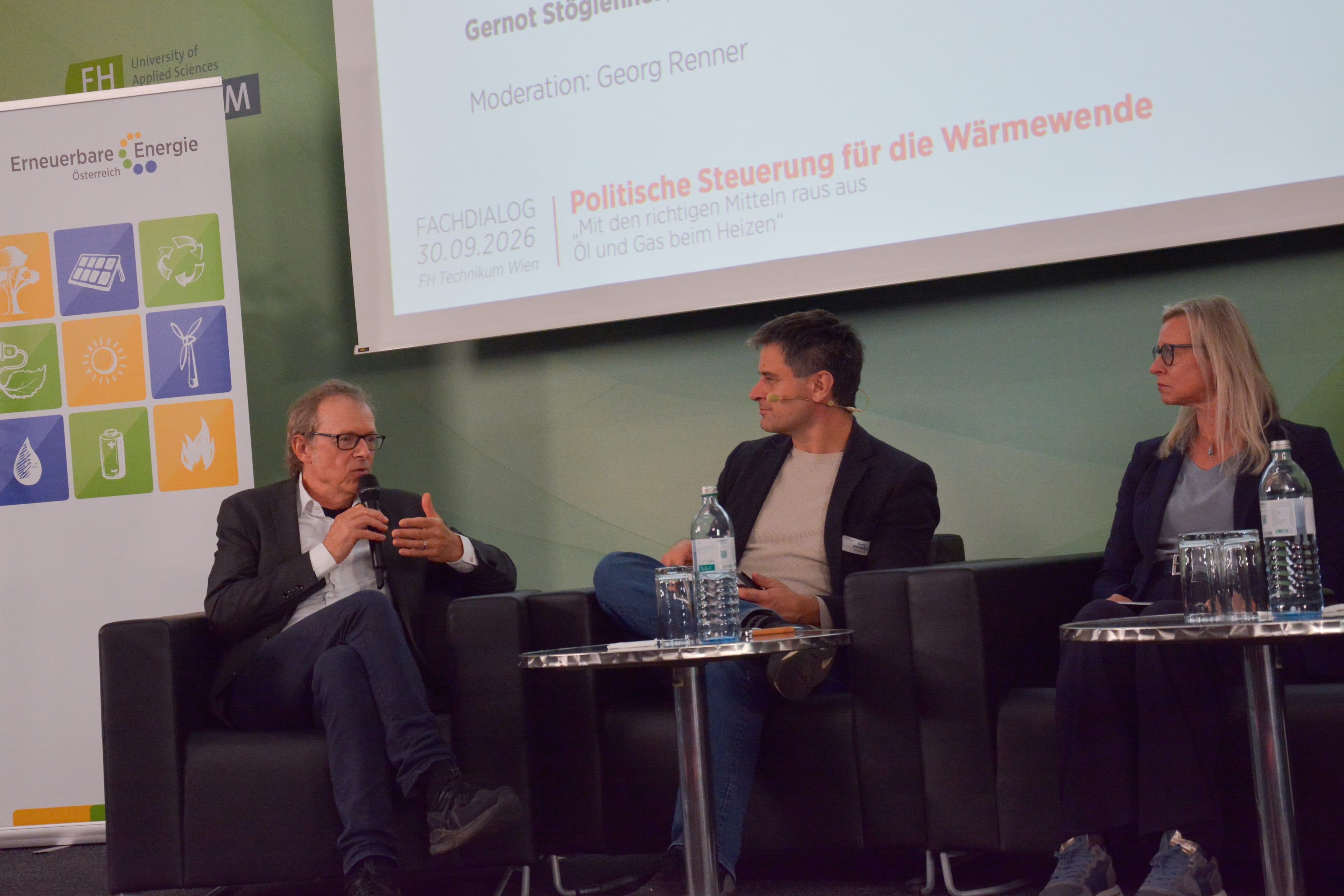 Drei Diskussionsteilnehmer sitzen während einer Diskussion über die Energiewende auf Stühlen auf einer Bühne, im Hintergrund ist eine Projektionswand zu sehen.