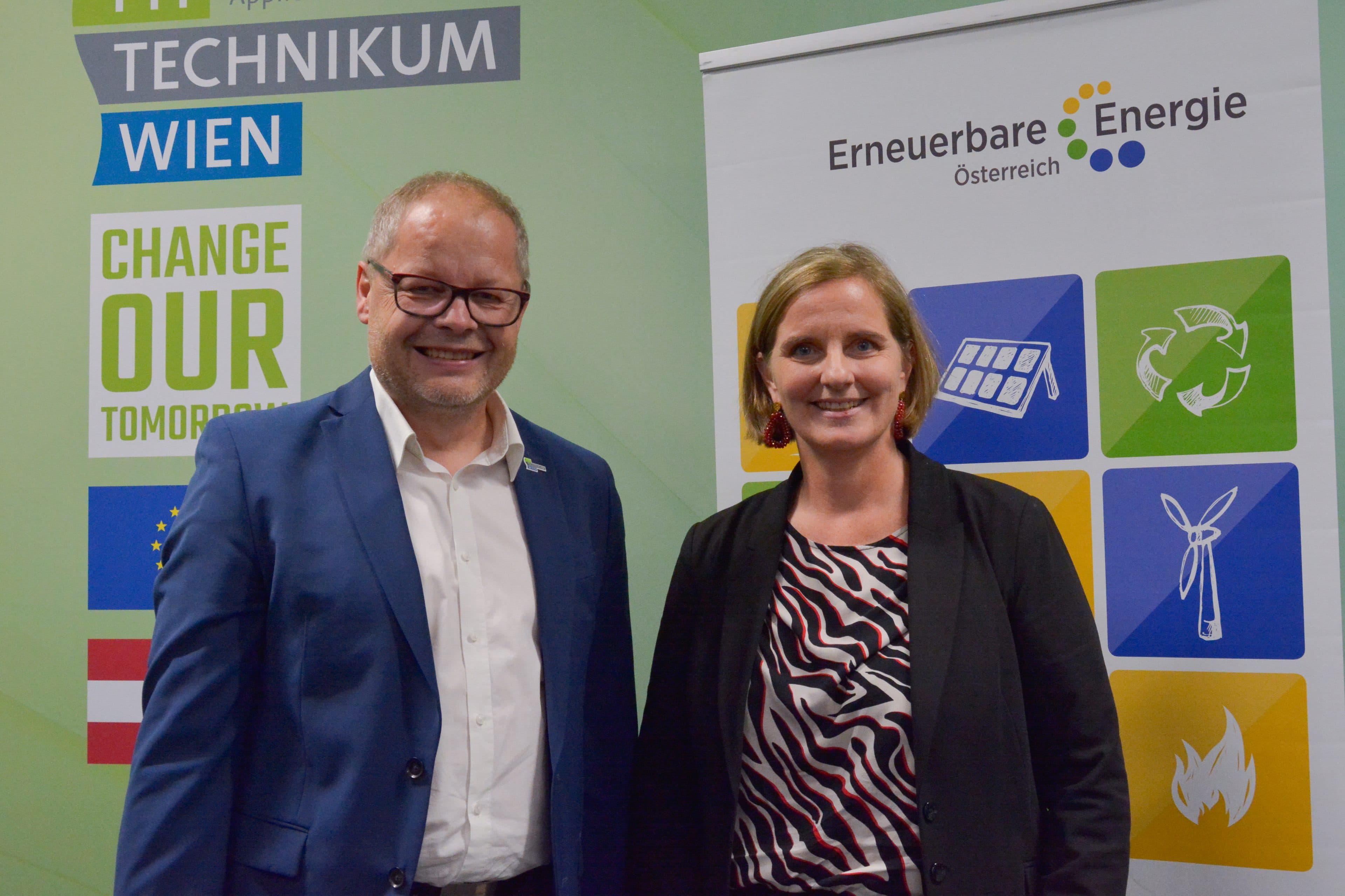Ein Mann und eine Frau stehen vor einem Veranstaltungsbanner von Erneuerbare Energie Österreich und dem Technikum Wien.