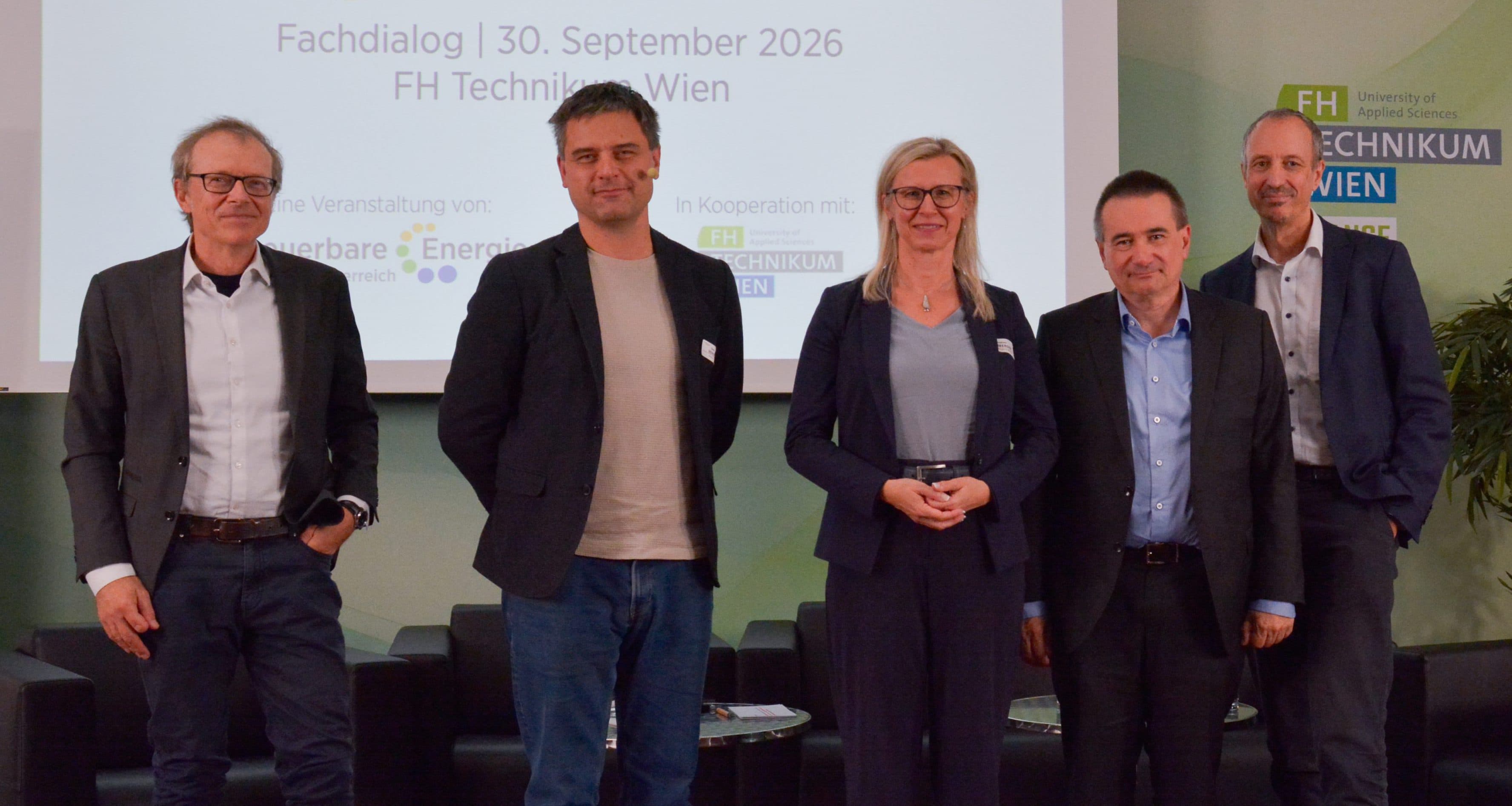 Fünf Personen stehen in einer Reihe auf einer Bühne vor einer Leinwand, auf der der Text Fachdialog | 30. September 2026 FH Technikum Wien zu lesen ist.