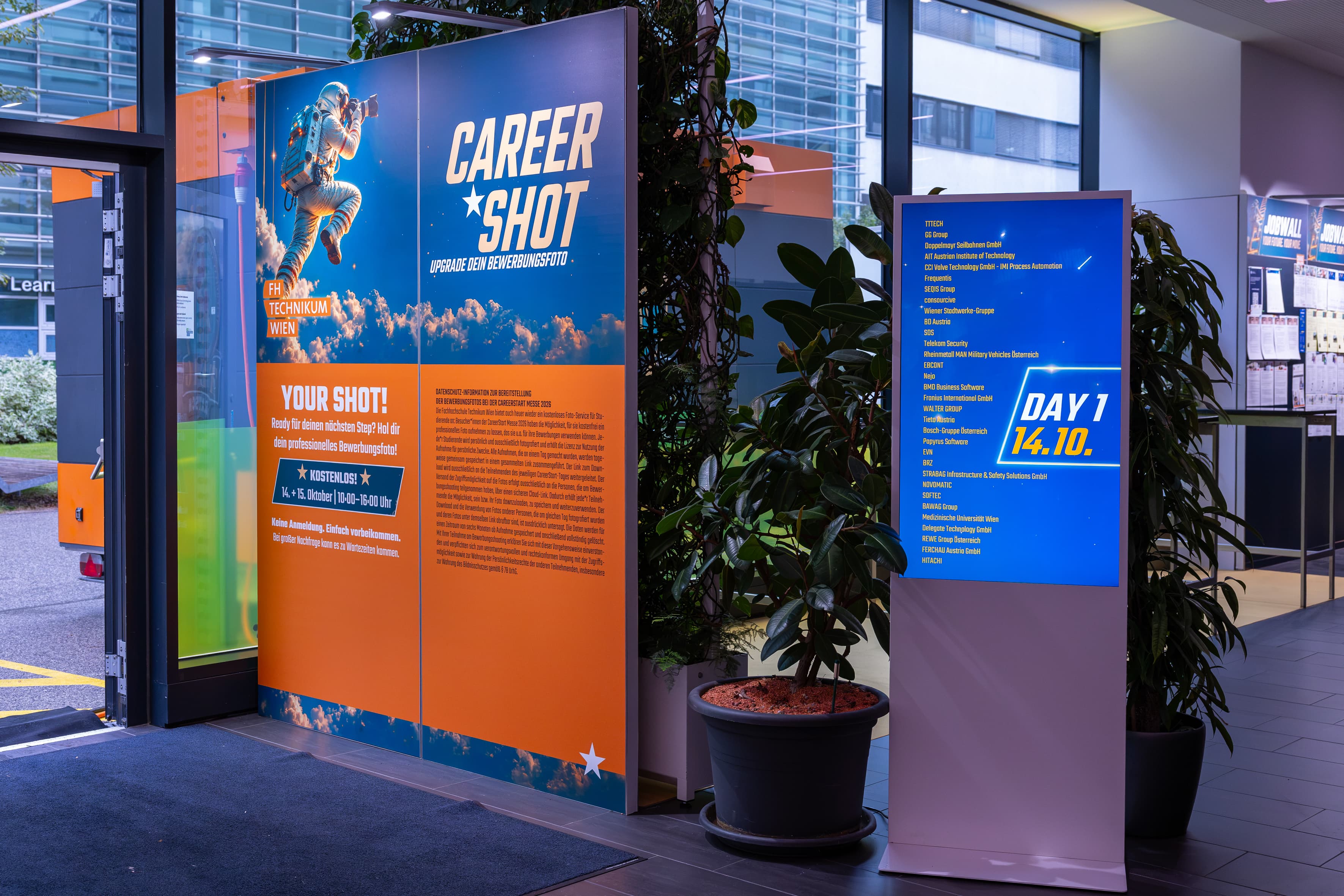 Eine große Veranstaltungsanzeige mit einer Astronauten-Grafik mit dem Titel Career Shot neben einem digitalen Bildschirm, auf dem die Firmennamen für Tag 1, den 14.10., angezeigt werden.