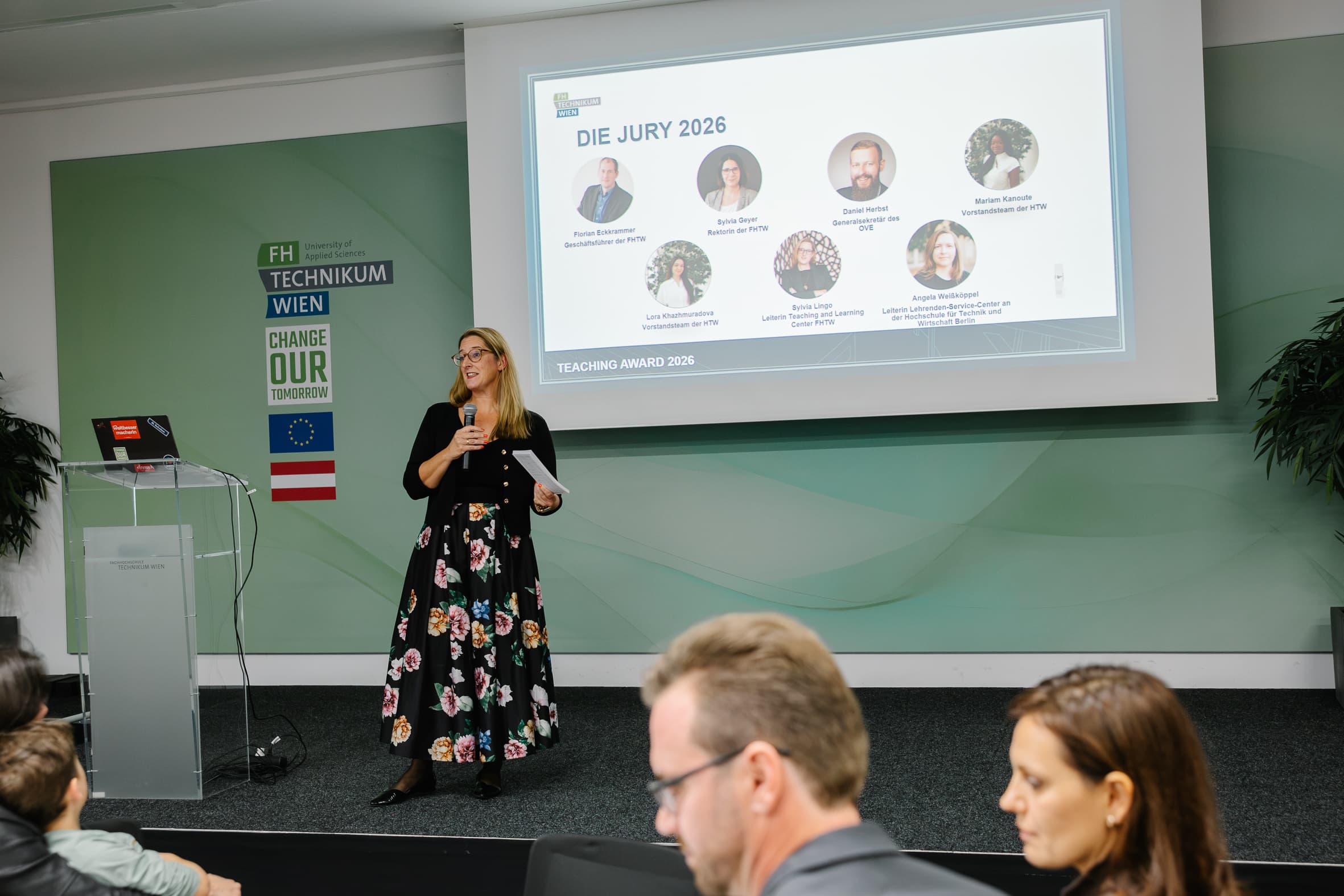 Eine Frau steht am Rednerpult und spricht zu den Zuhörern vor einer Leinwand, auf der die Jury 2026 des FH Technikum Wien-Lehrpreises zu sehen ist.