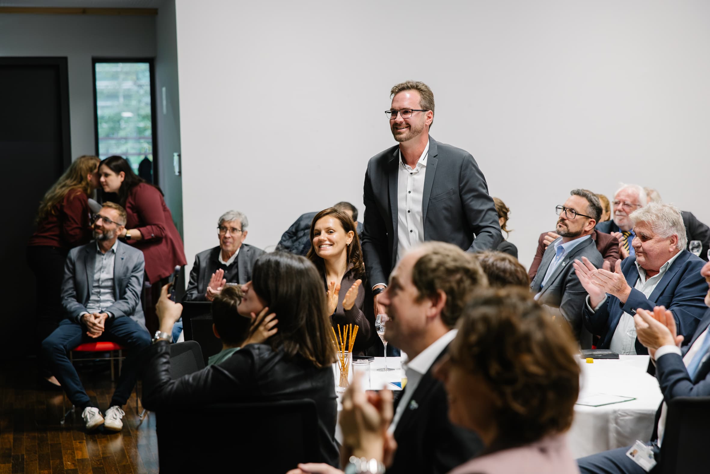 Ein Mann im Anzug steht in einem überfüllten Konferenzraum, während das Publikum applaudiert.