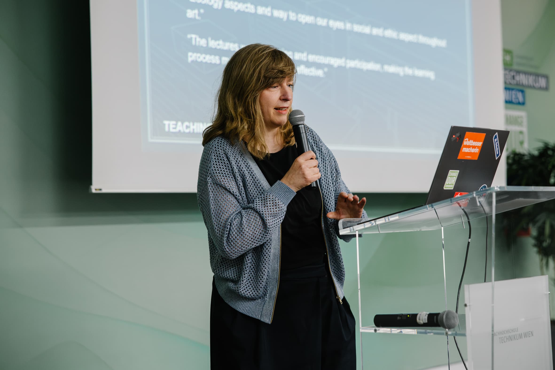 Eine Frau, die an einem Rednerpult spricht, im Hintergrund ein Laptop und eine Leinwand.
