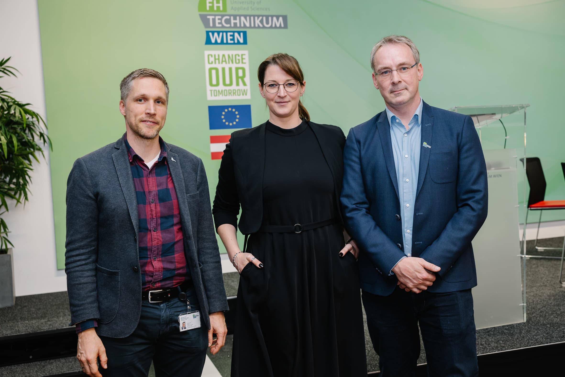 Drei Personen stehen vor einer grünen Wand mit dem Logo des Technikum Wien.