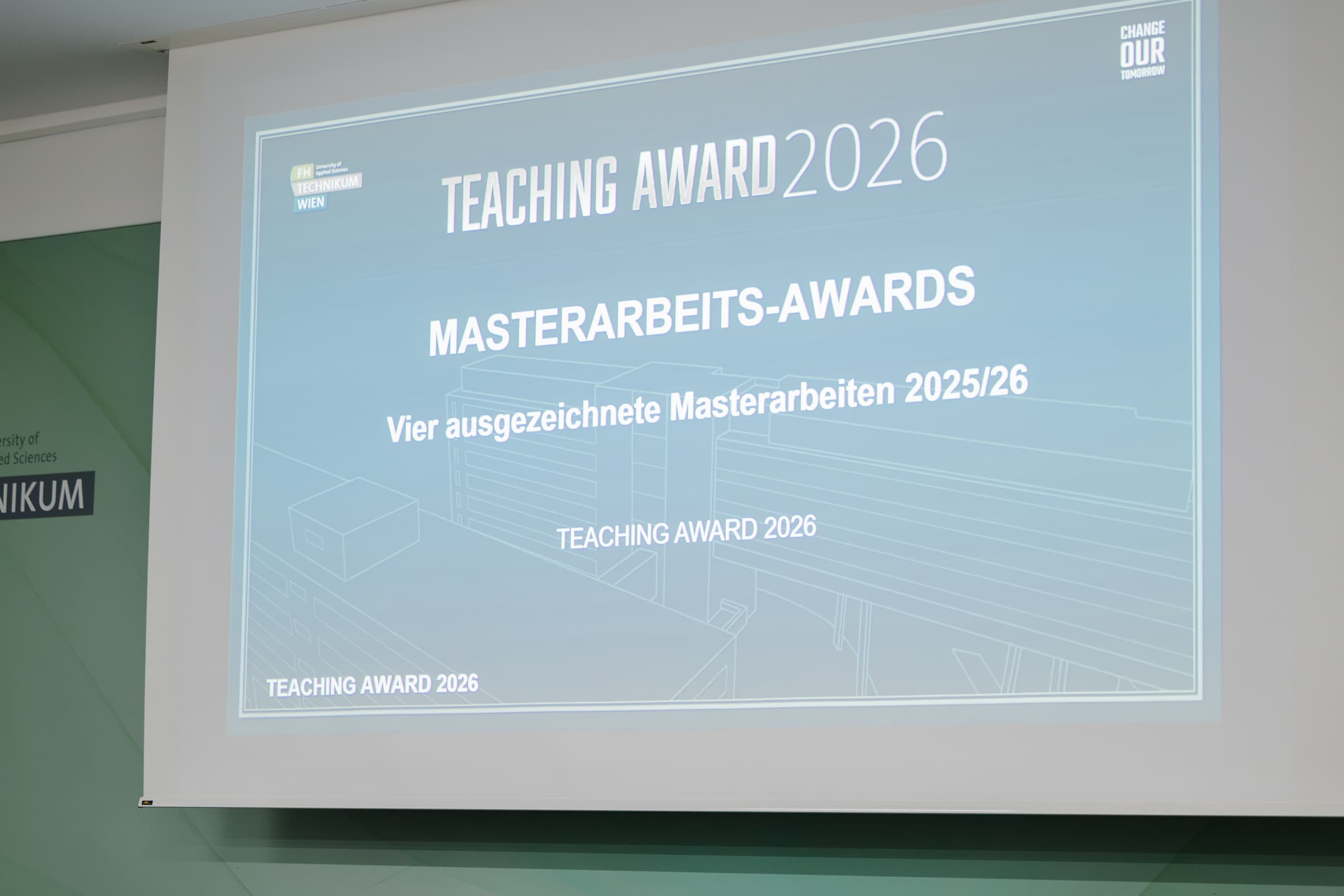 Projektionsleinwand mit der Aufschrift TEACHING AWARD 2026 MASTERARBEITS-AWARDS Vier ausgezeichnete Masterarbeiten 2025/26 und dem Logo der Fachhochschule Technikum Wien.