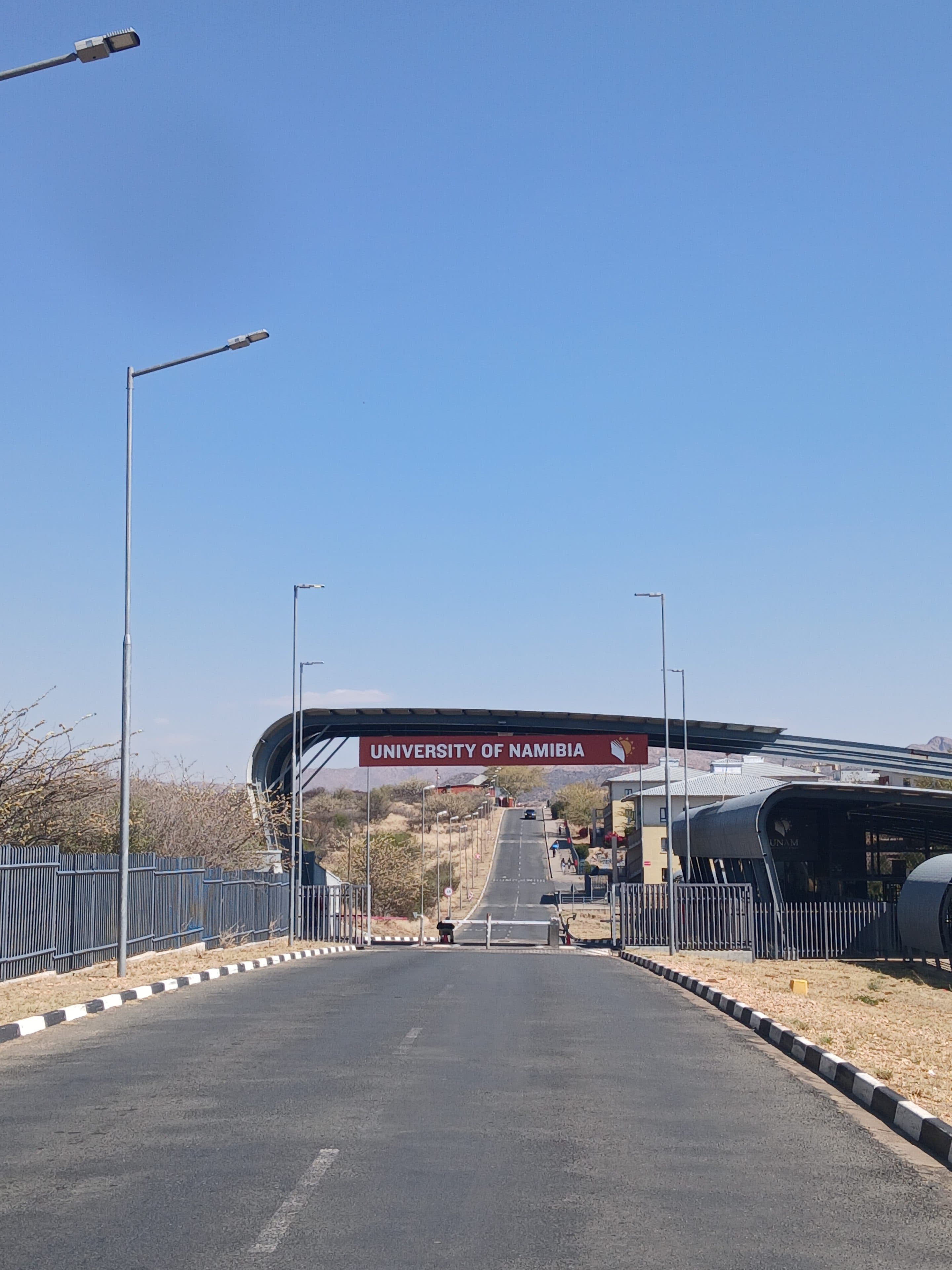 Ein gewölbtes Tor, das eine Straße überspannt, mit einem Schild, auf dem University of Namibia steht.